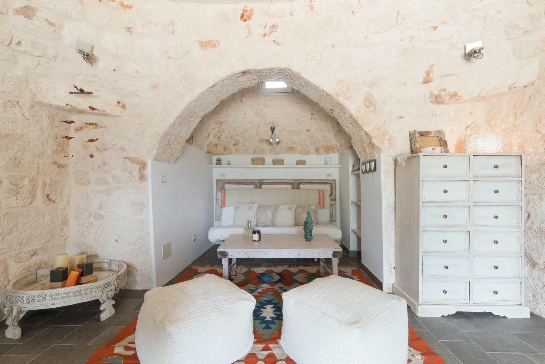 A rustic bedroom with a bed beneath a stone arch and a patterned rug.