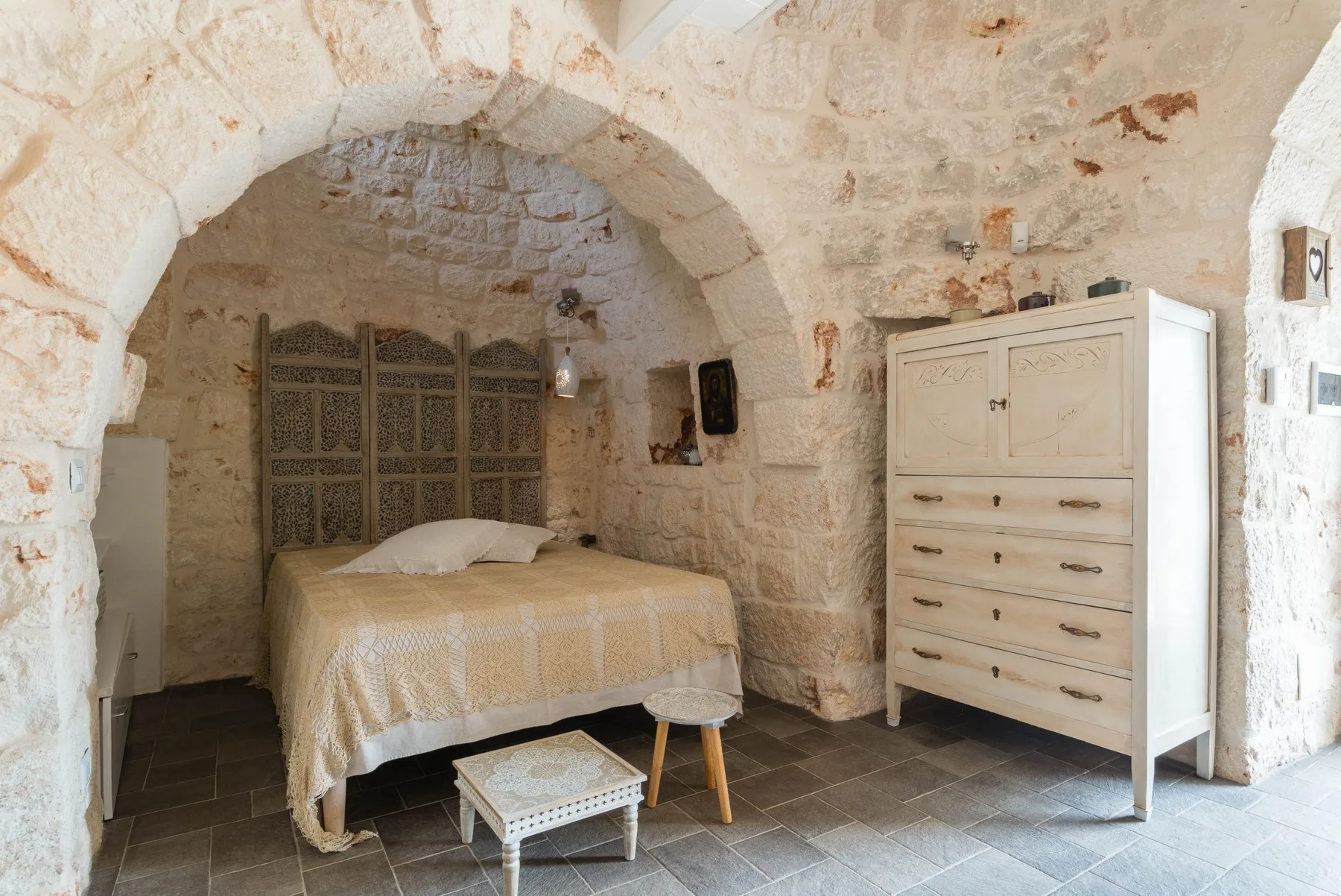 A bedroom with a bed beneath a stone arch and a chest of drawers.