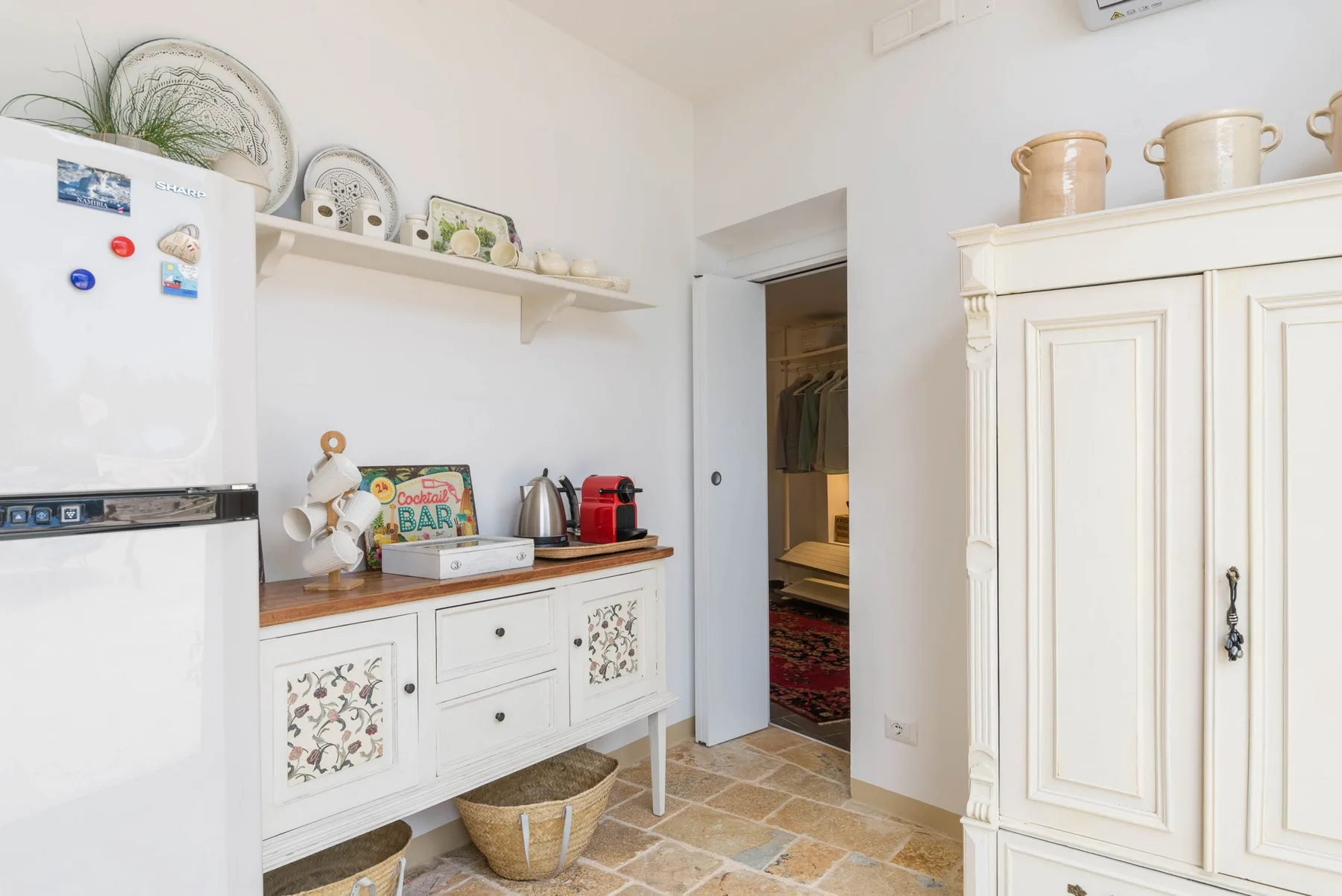 A bright kitchen with white cabinets and a refrigerator beside an open doorway.