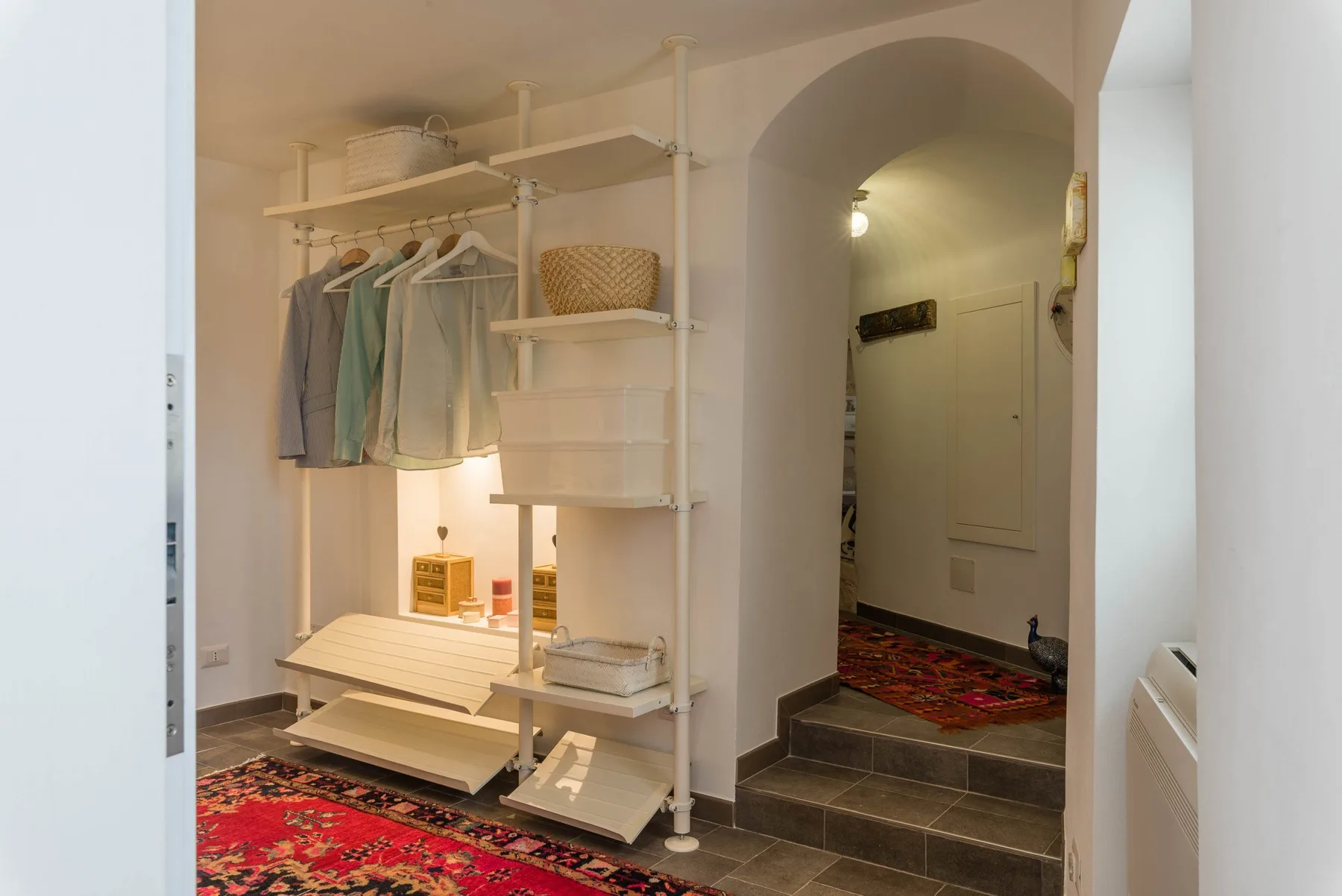 A clothing storage area with hanging garments and shelving sits beside an arched hallway.