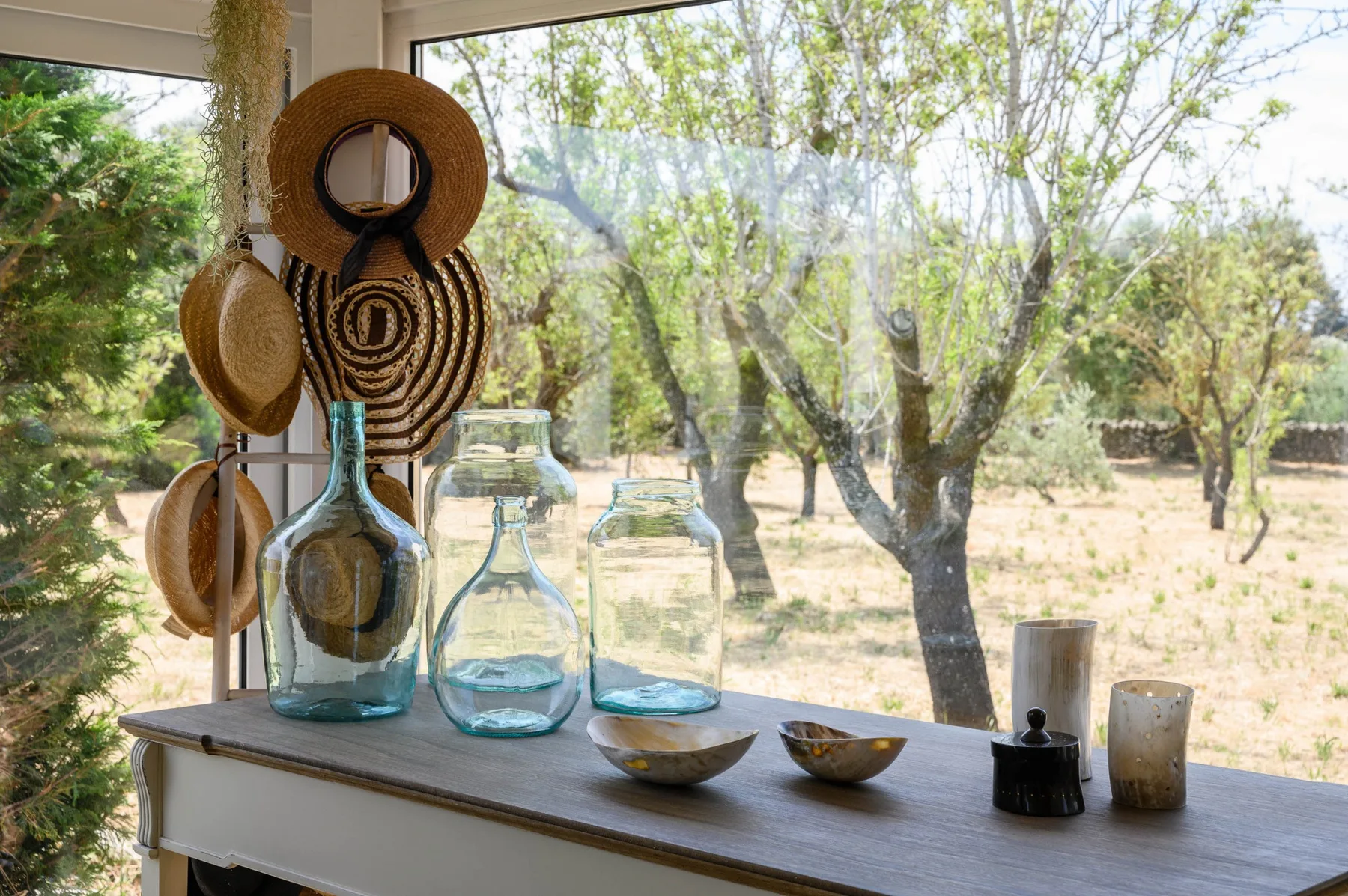 A bright interior window overlooks a wooded landscape, with glass vases on the sill.