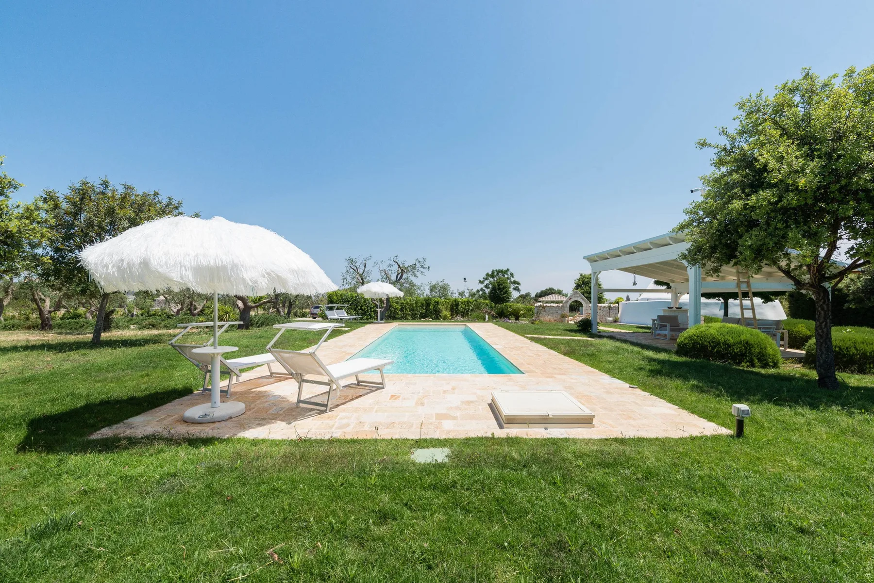 An outdoor swimming pool is surrounded by lawn, loungers, and shade umbrellas.