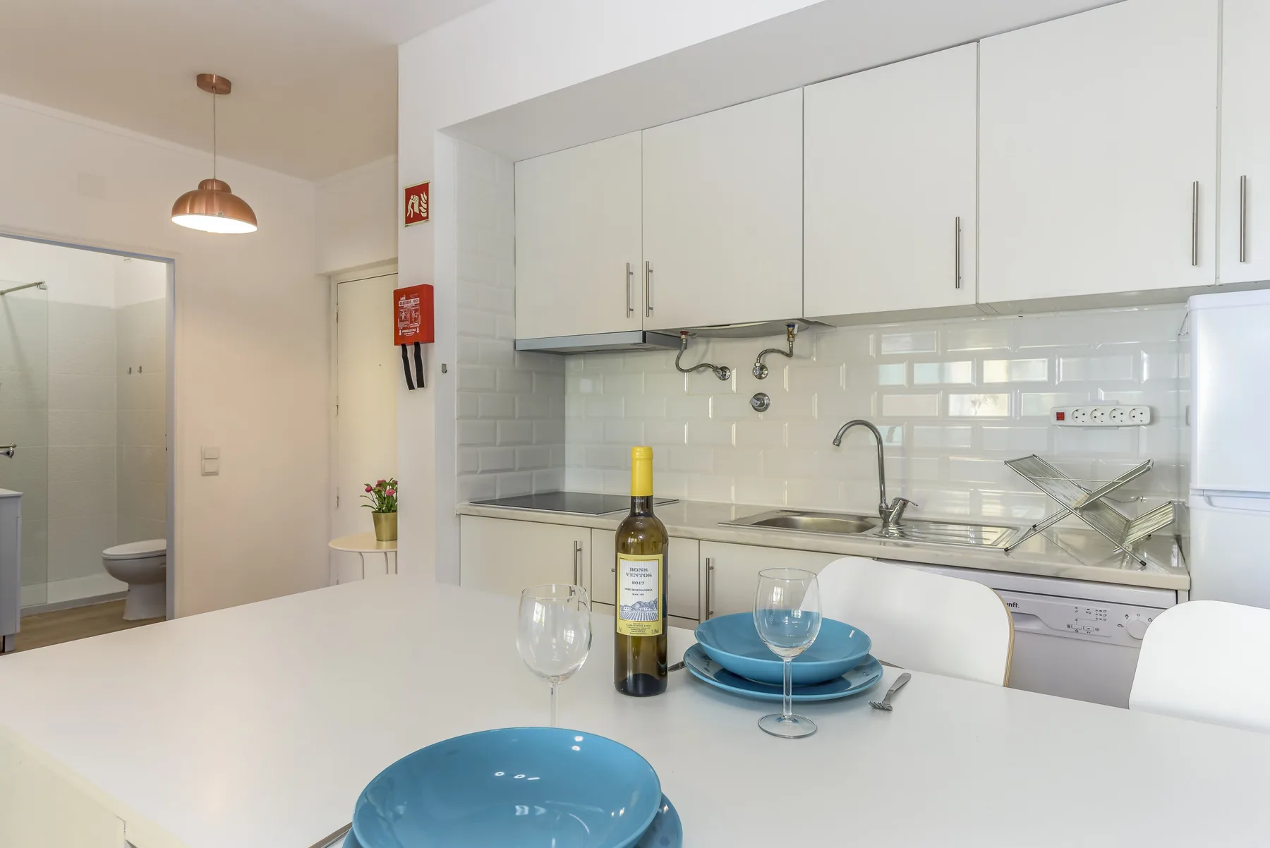 A bright kitchen and dining area with a white counter, blue dishes, and upper cabinets.