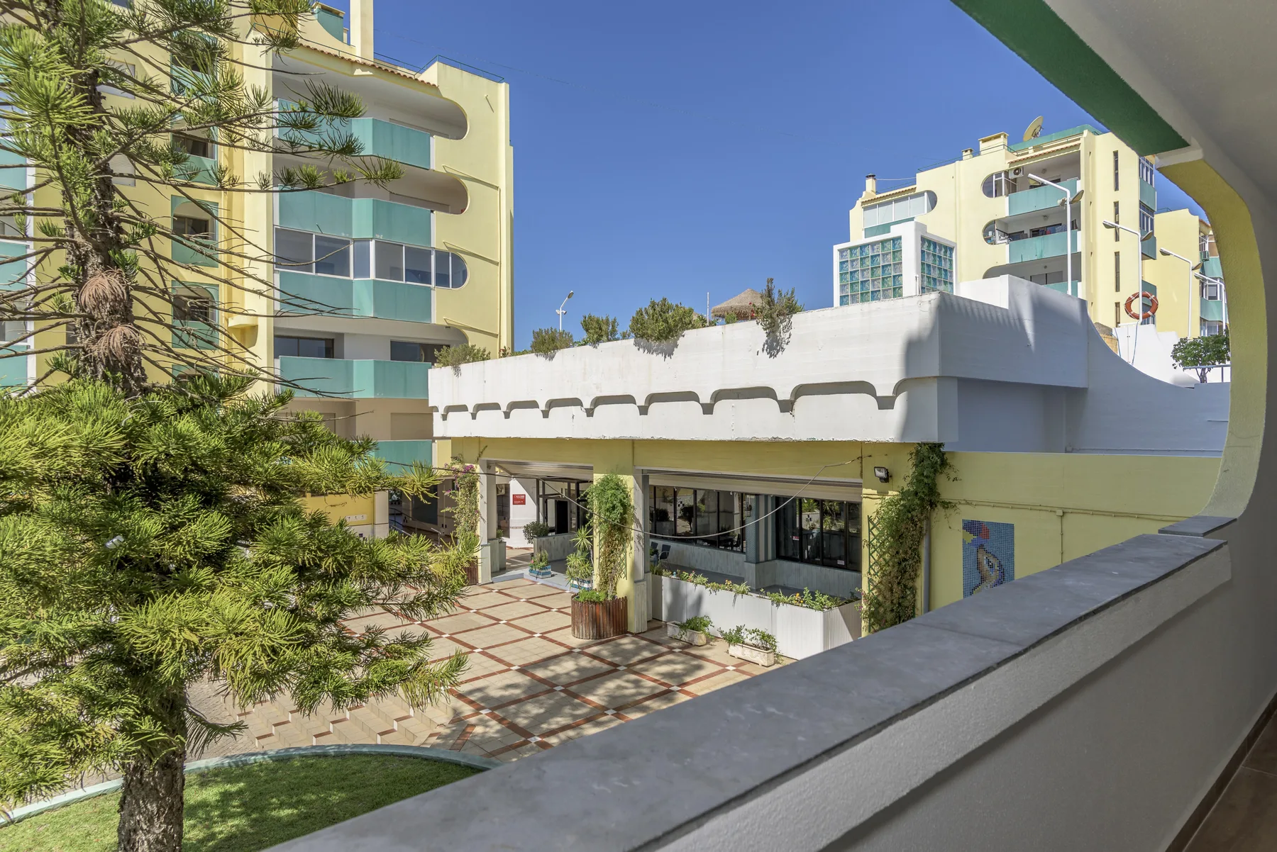 An apartment complex surrounds a paved courtyard with trees and balconies.