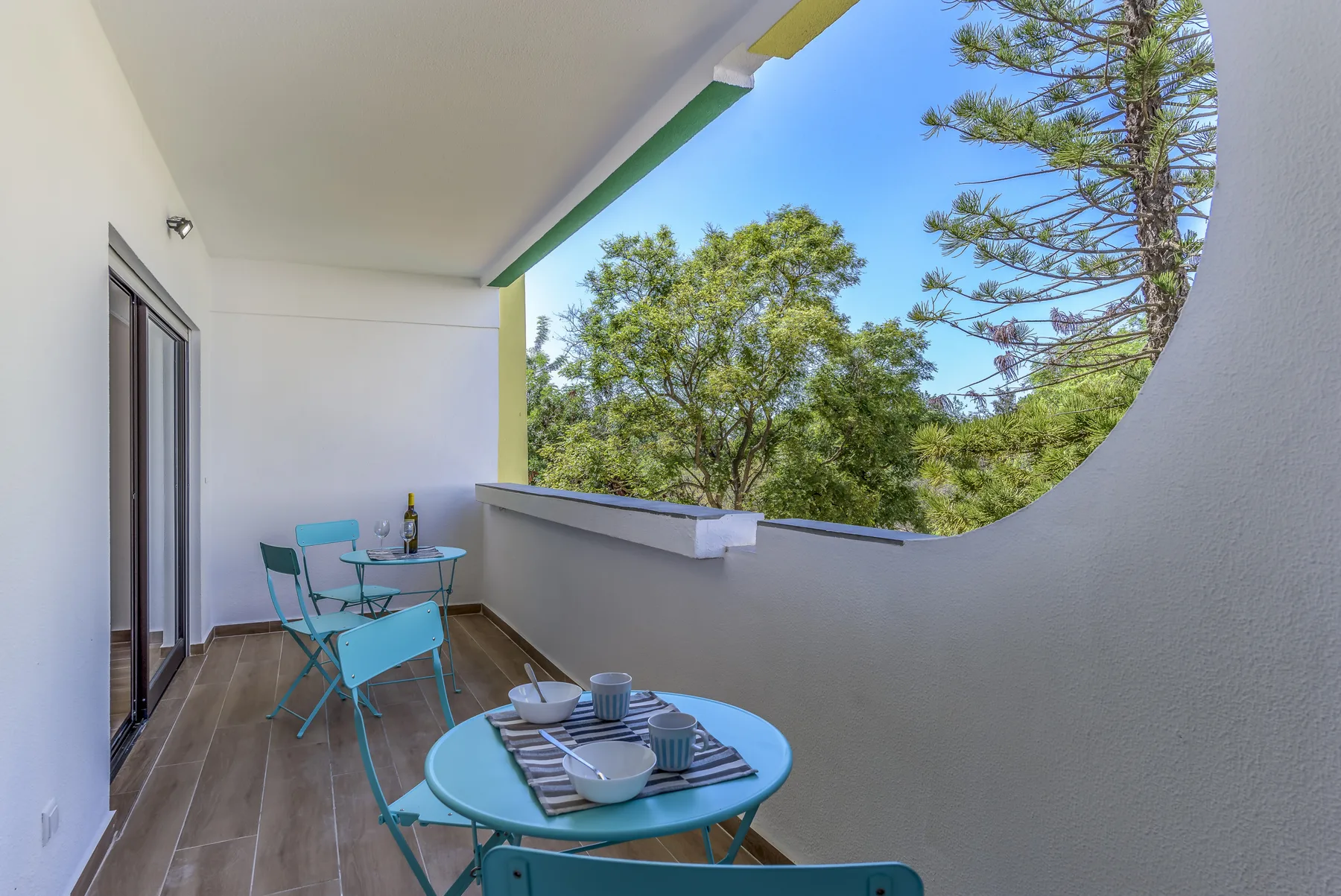 A balcony with turquoise outdoor seating and trees visible beyond the railing.