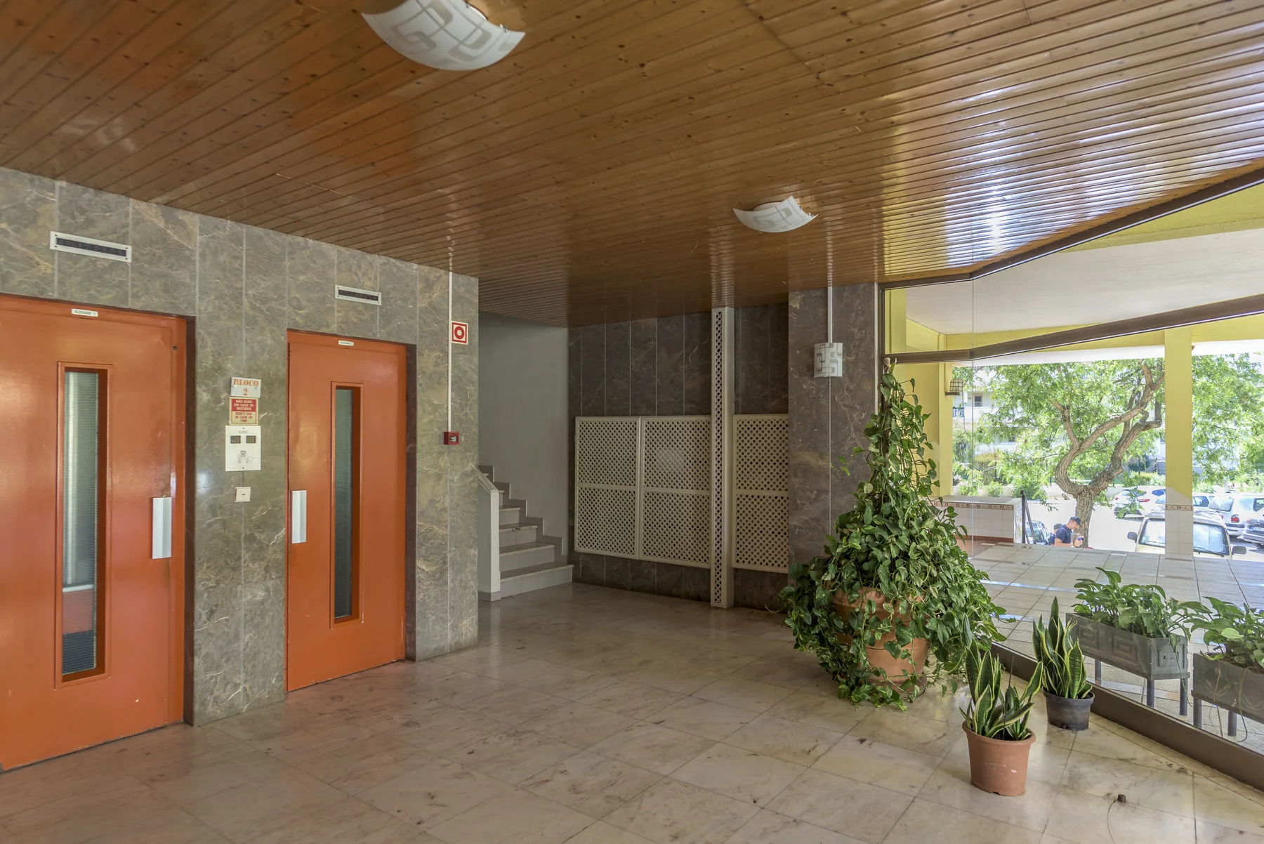 A tiled building lobby with elevators, stairs, and a glazed entrance area.