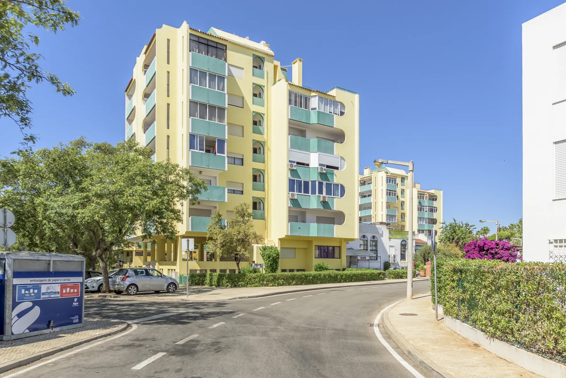 A curved street runs past yellow apartment buildings under a clear blue sky.