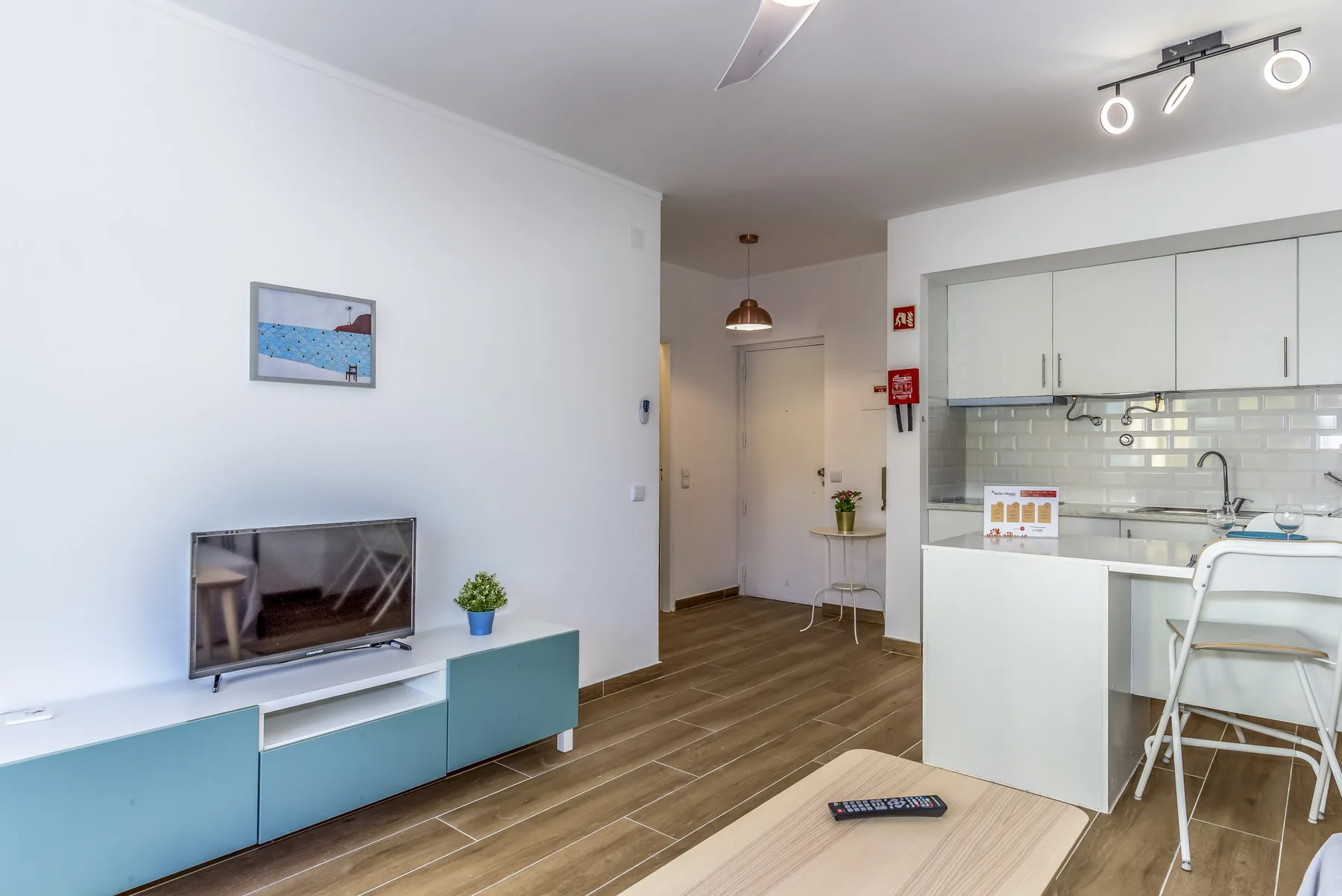 A bright open-plan living area with a television beside a kitchen.