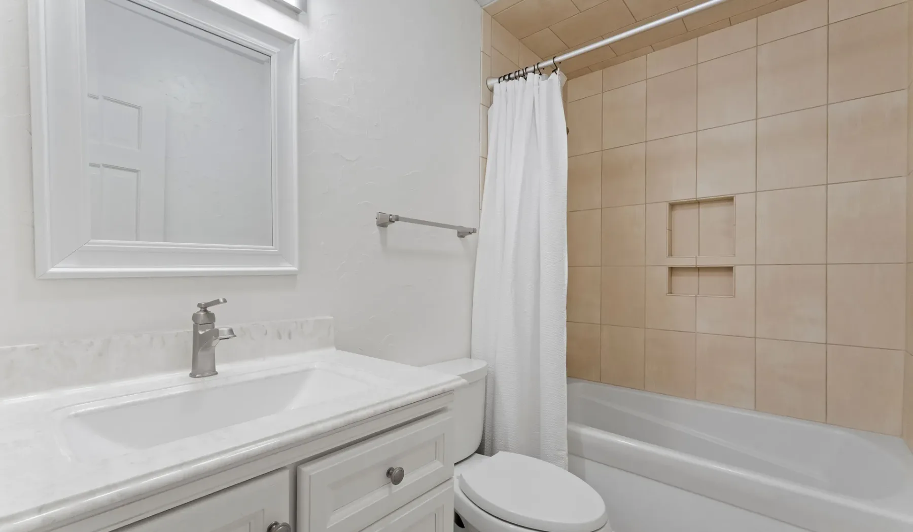 Un baño luminoso con lavabo, espejo, inodoro y bañera detrás de una cortina de ducha.