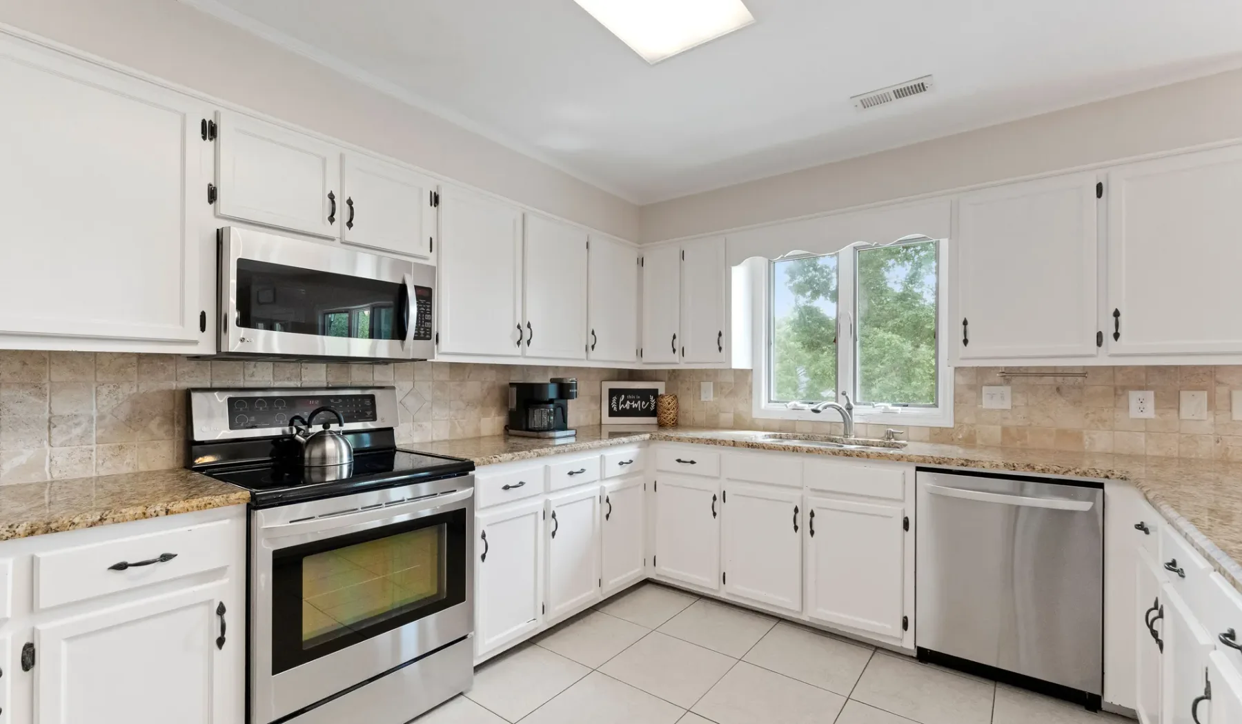 Una cocina luminosa con gabinetes blancos, salpicadero de azulejos y una ventana sobre el fregadero.