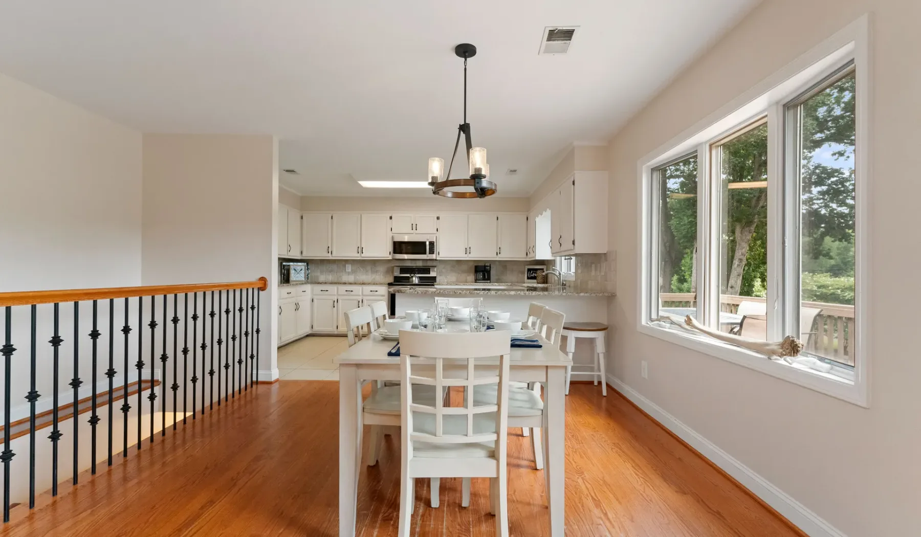 Un comedor abierto con una mesa blanca junto a la cocina y grandes ventanas.