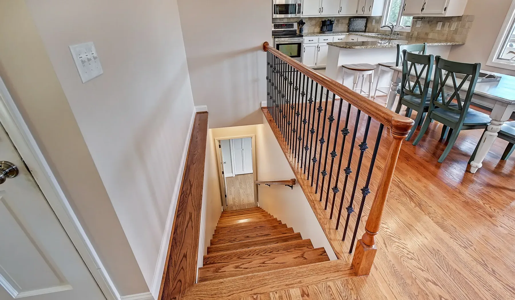 Una escalera de madera desciende junto a un comedor y una cocina abierta.