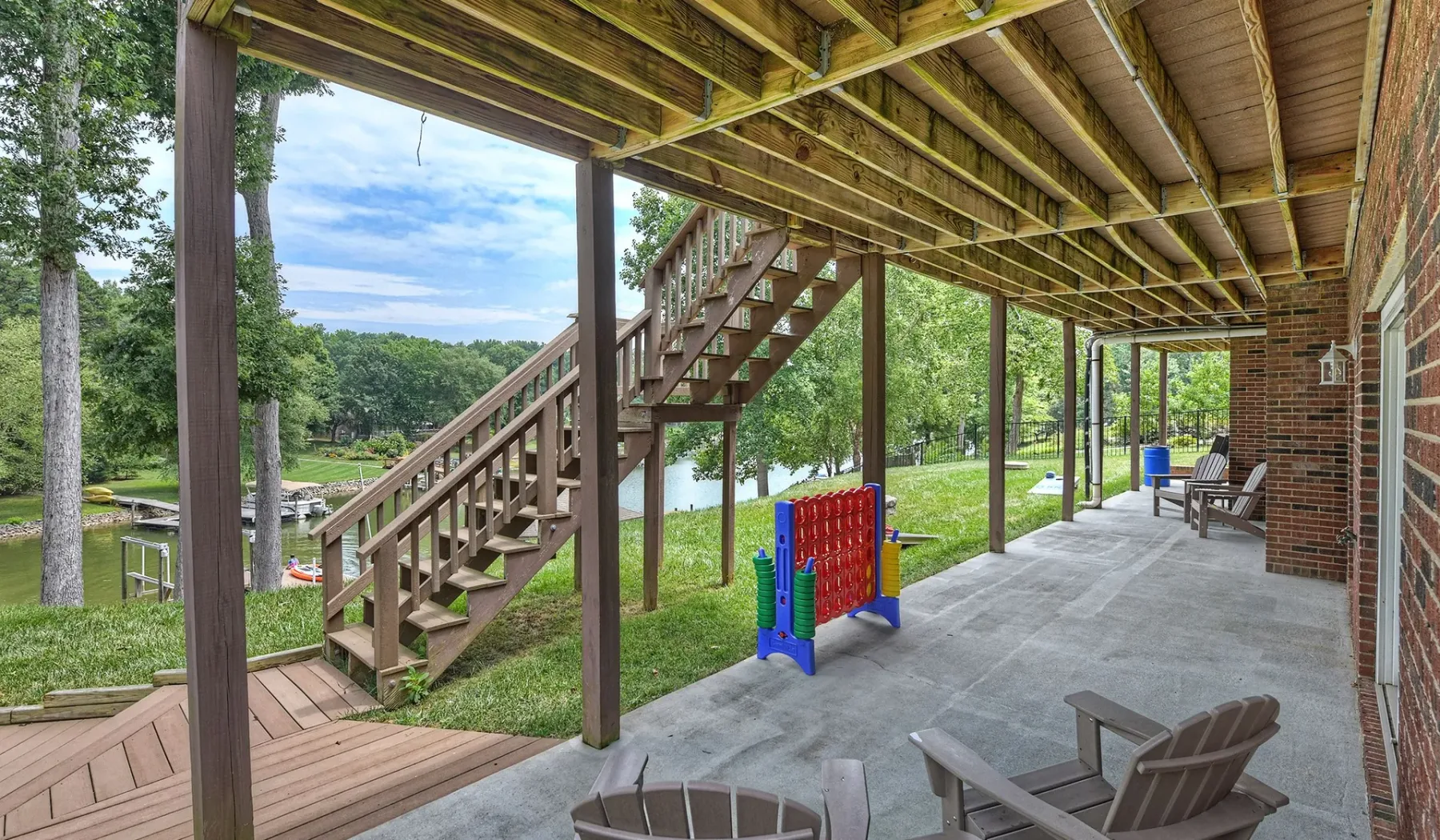 Un patio cubierto con asientos al aire libre y una escalera de madera frente a un jardín verde.