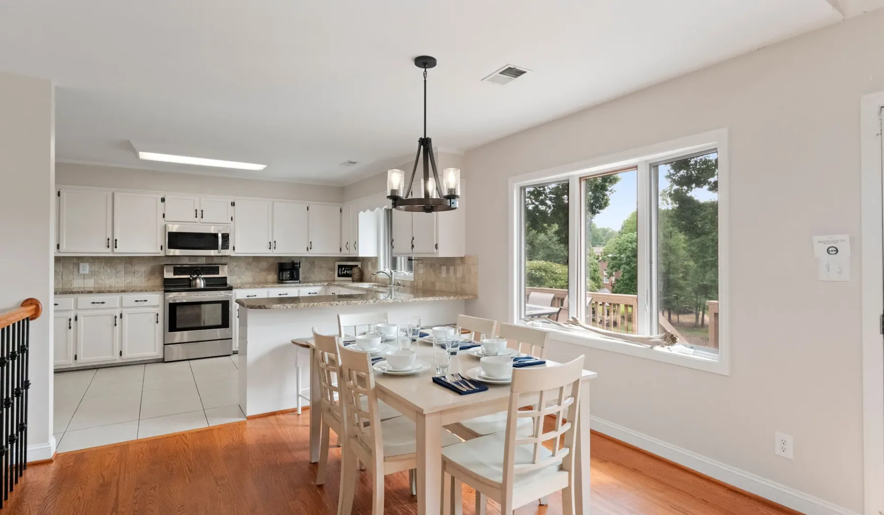 Una cocina luminosa y zona de comedor con la mesa puesta junto a grandes ventanas.