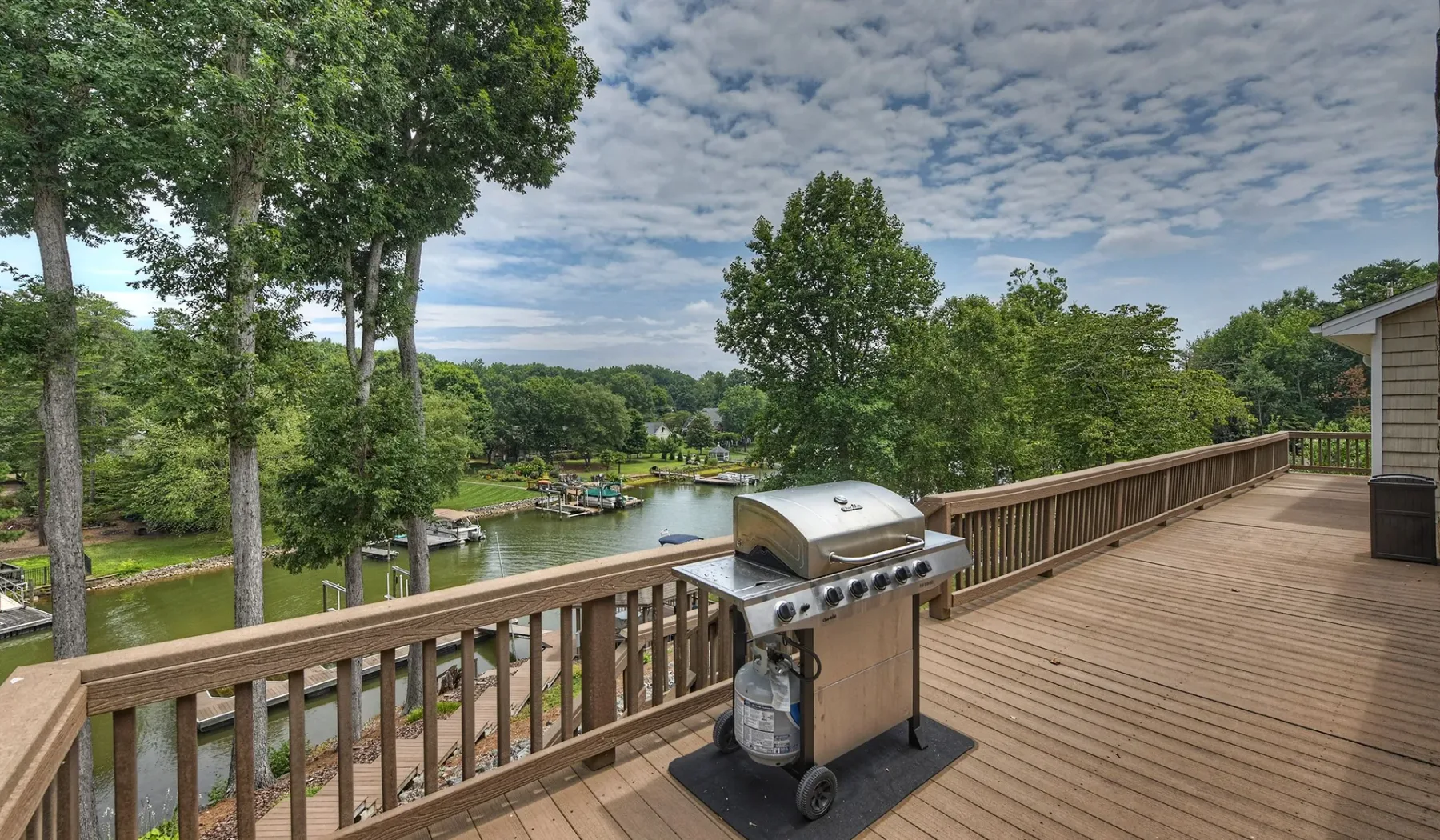 Una terraza de madera da a un río bordeado de árboles, con una parrilla junto a la barandilla.