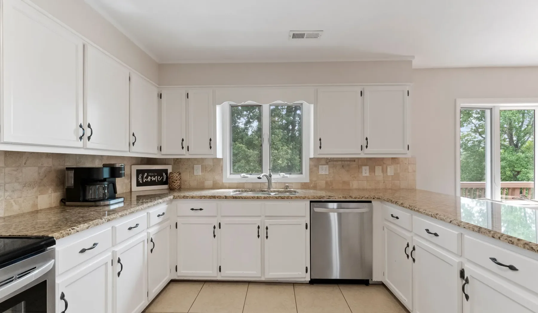 Una cocina luminosa con gabinetes blancos, salpicadero de azulejos y electrodomésticos de acero inoxidable.