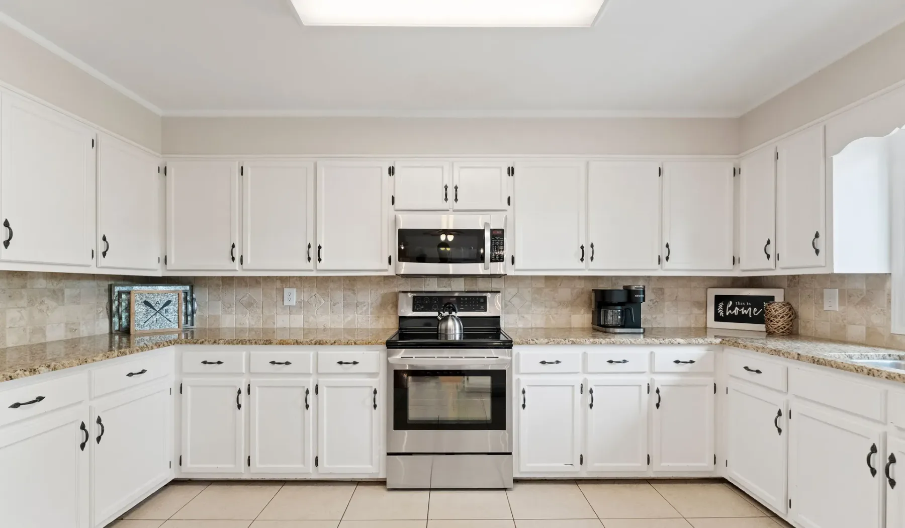 Una cocina luminosa con gabinetes blancos, salpicadero de azulejos y electrodomésticos de acero inoxidable.
