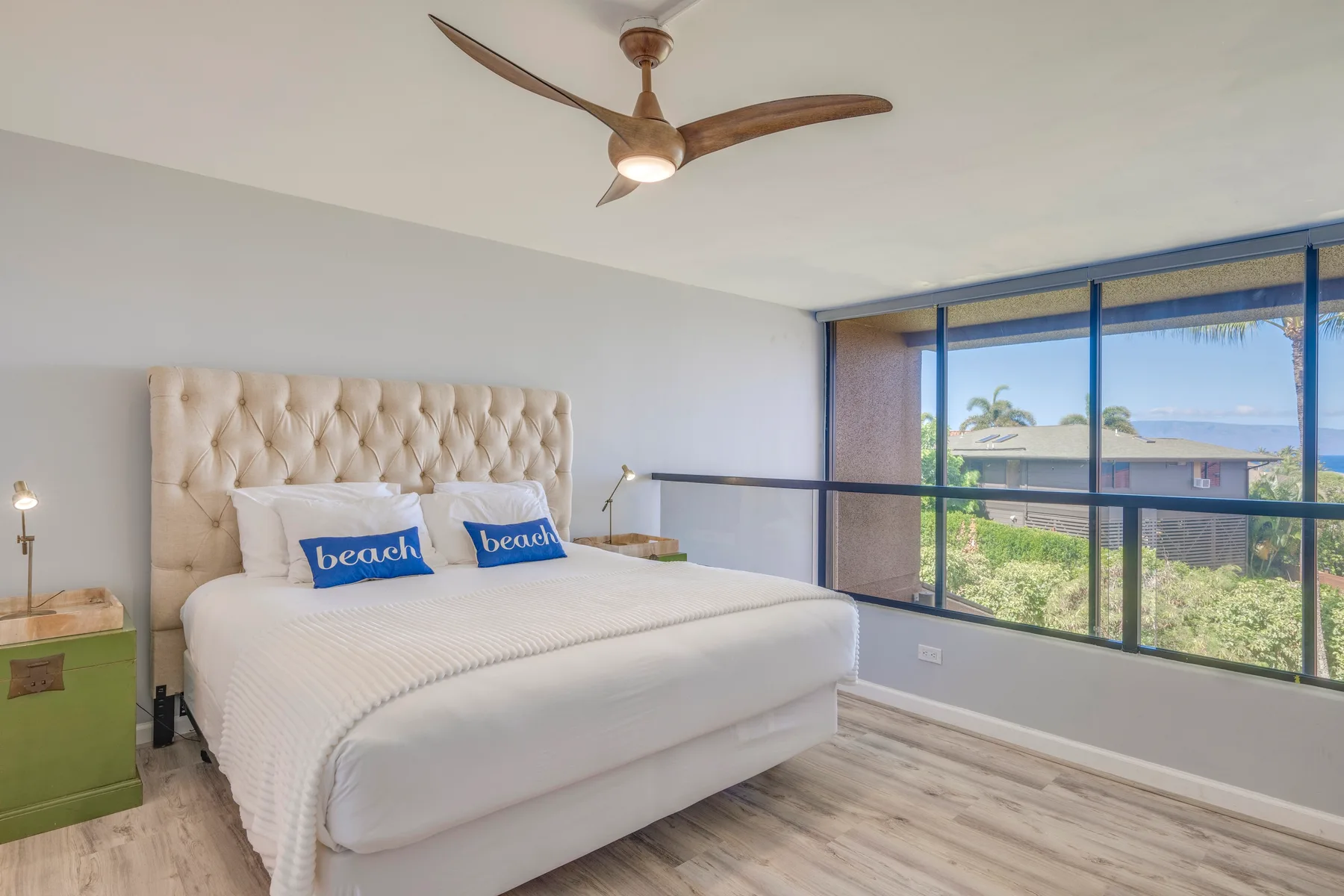 A bright bedroom with a large bed beside wide windows overlooking greenery.