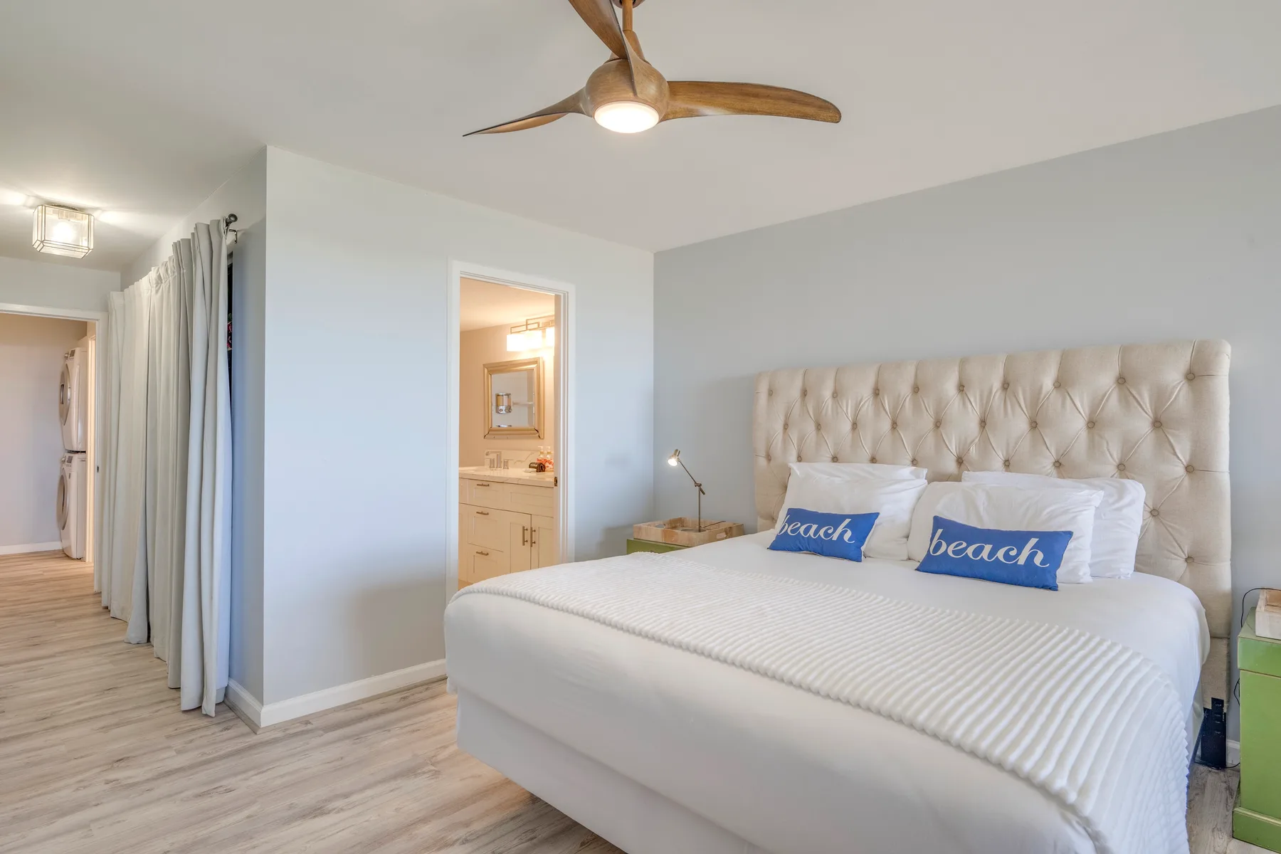 A bright bedroom with a large bed, blue accent pillows, and a ceiling fan.