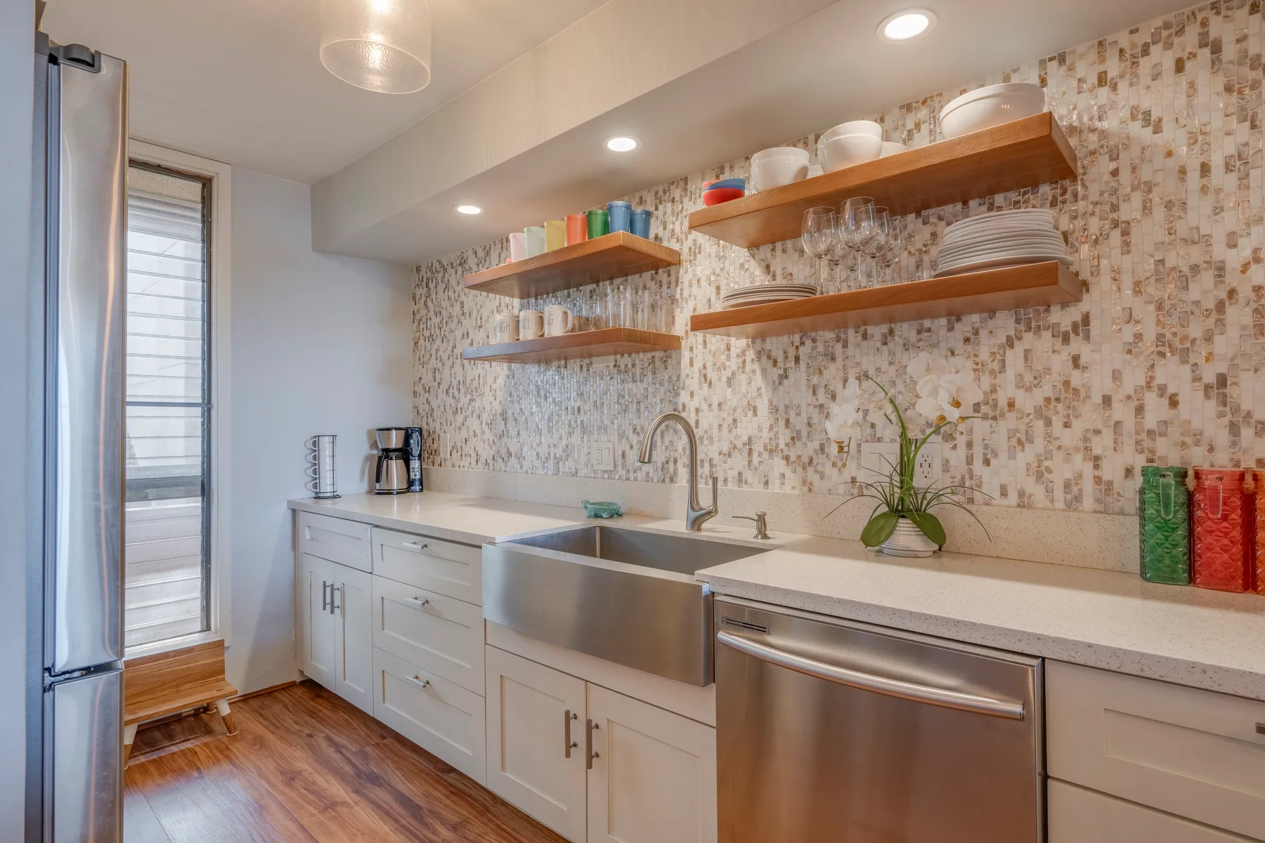 A bright kitchen with a long countertop, sink, and open shelves.