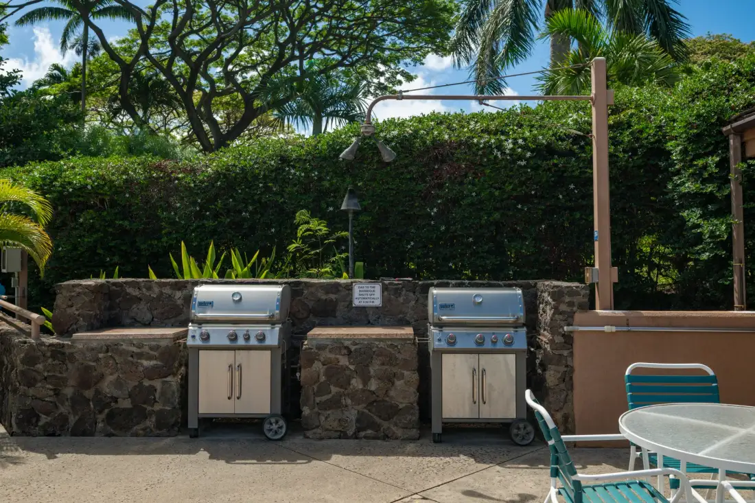 An outdoor cooking area with two grills beside a patio dining table.