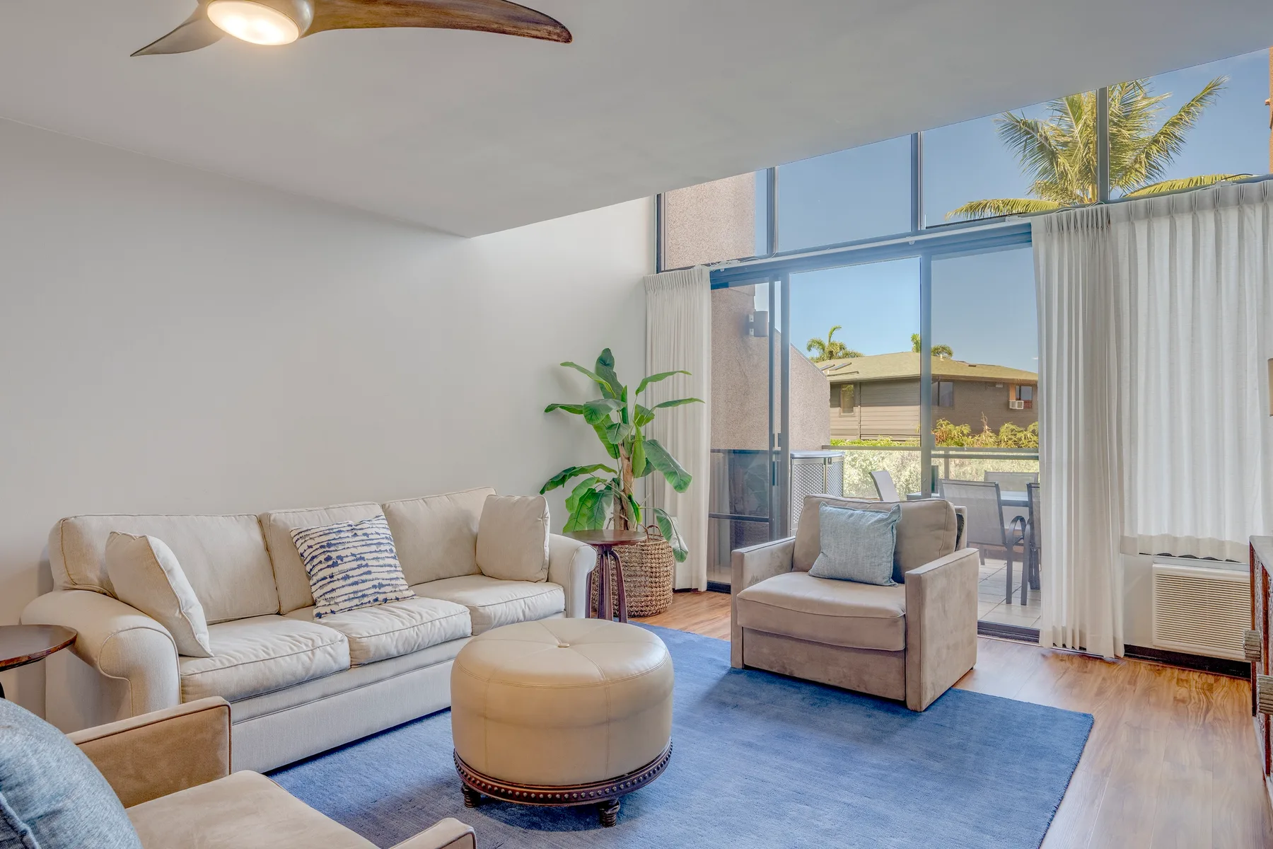 A bright living room with seating arranged around a round ottoman and blue rug.