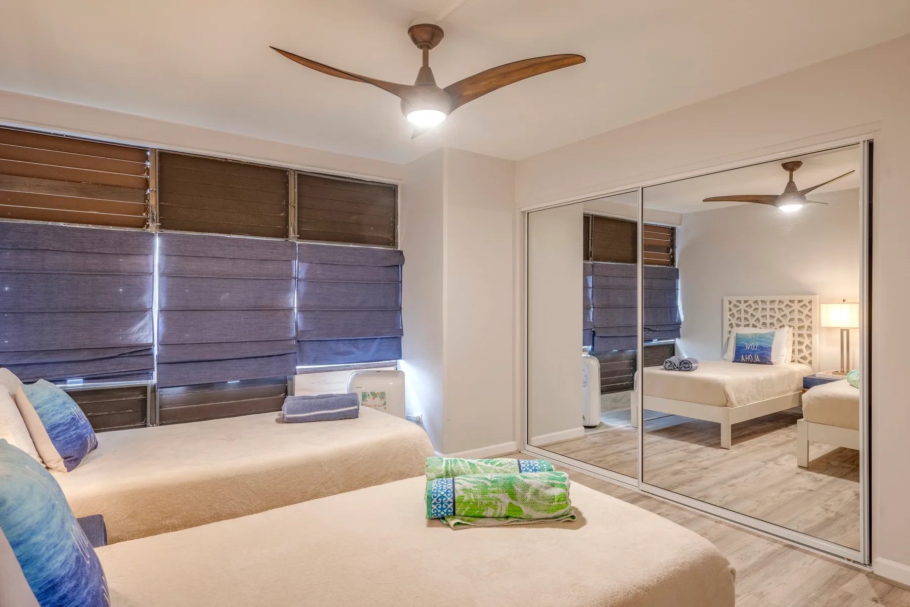 A bedroom with beds beneath wide windows and mirrored closet doors.