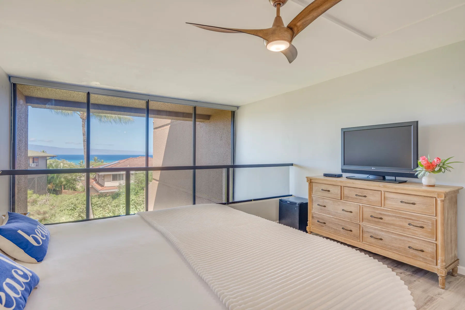 A bedroom with a bed, wide windows, and a television on a wooden dresser.