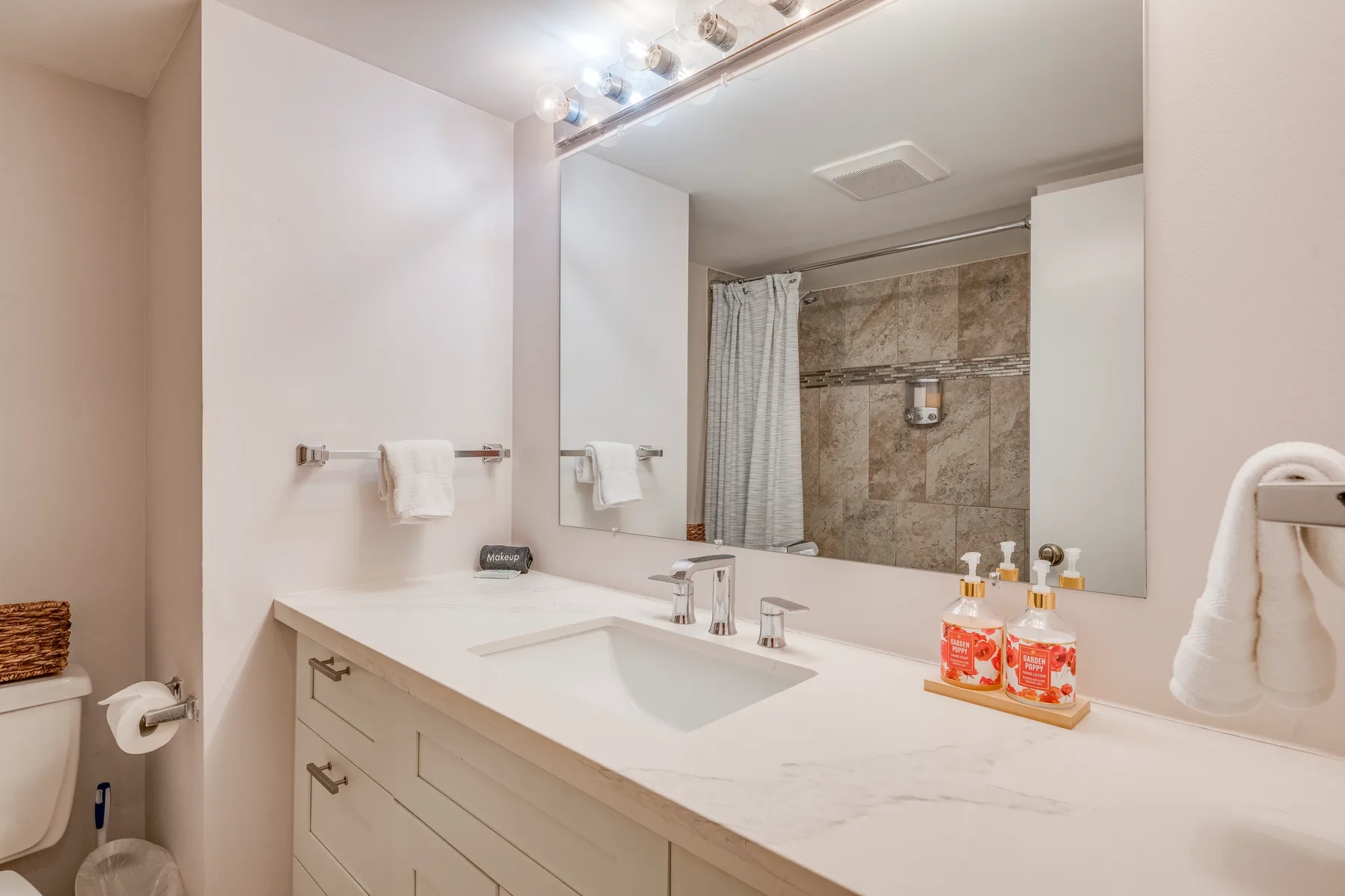 A bathroom vanity with a sink and a large mirror faces a tiled shower.