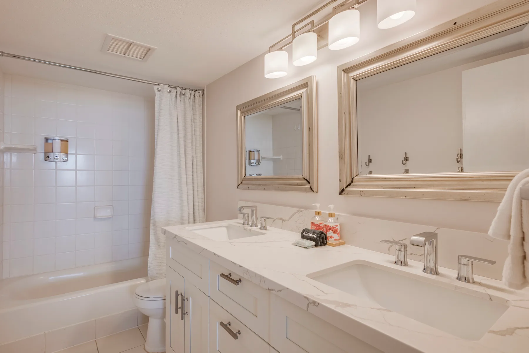 A bathroom with a double sink vanity, mirrors, and a bathtub behind a shower curtain.
