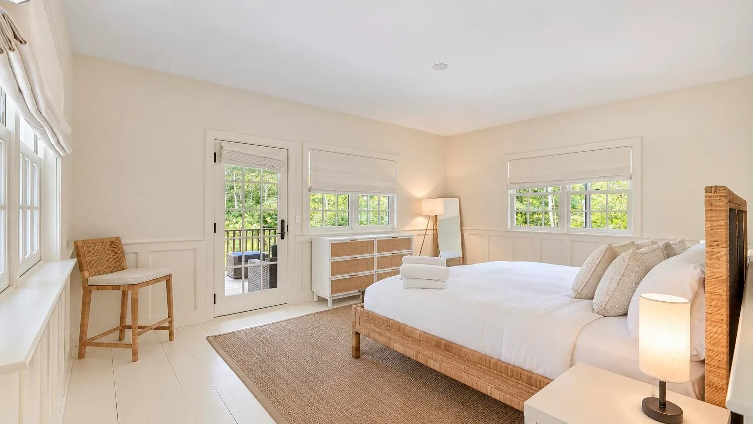 A bright bedroom with a large bed, bedside lamps, and a woven rug.
