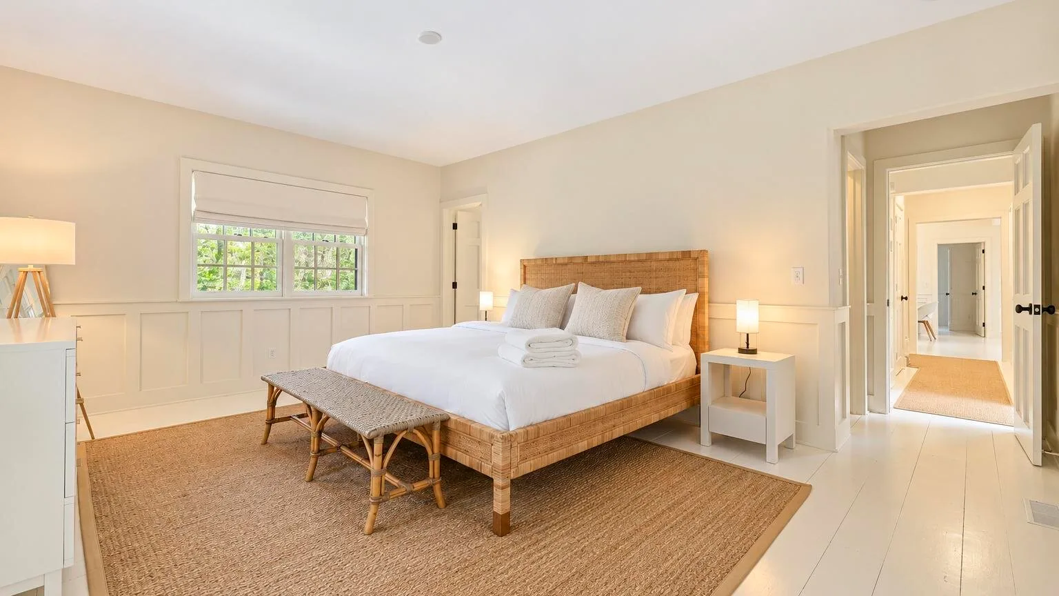 A bright bedroom with a neatly made bed and a window overlooking greenery.