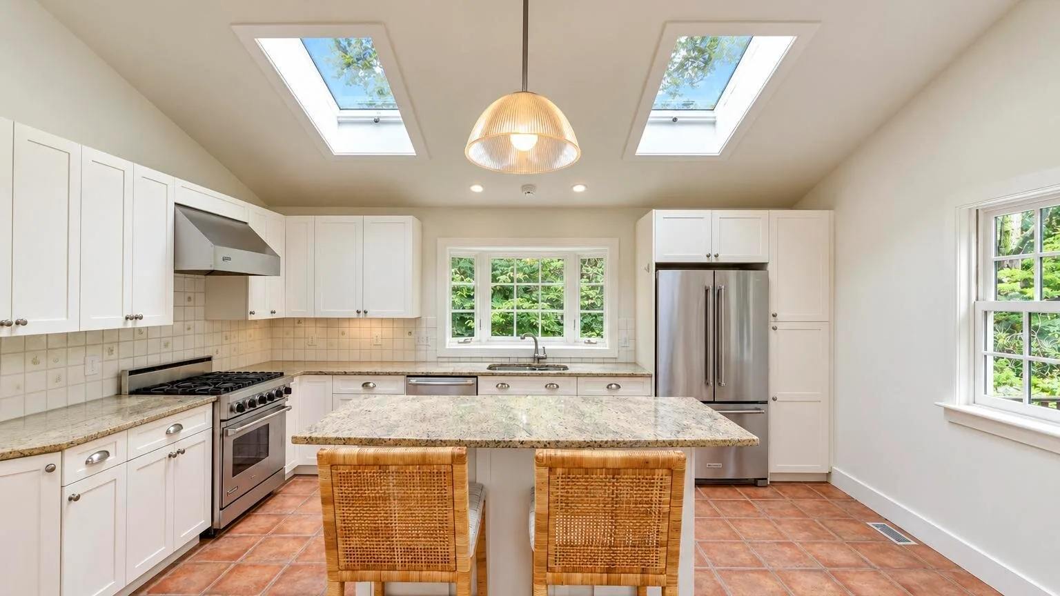 A bright kitchen with a central island, white cabinetry, and skylights.