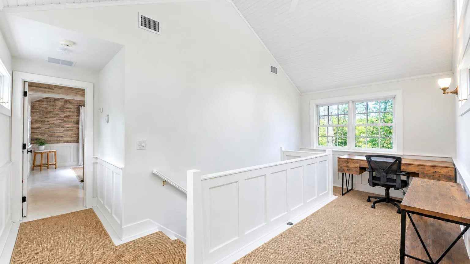A bright upstairs workspace with desks and a view through the stair railing.
