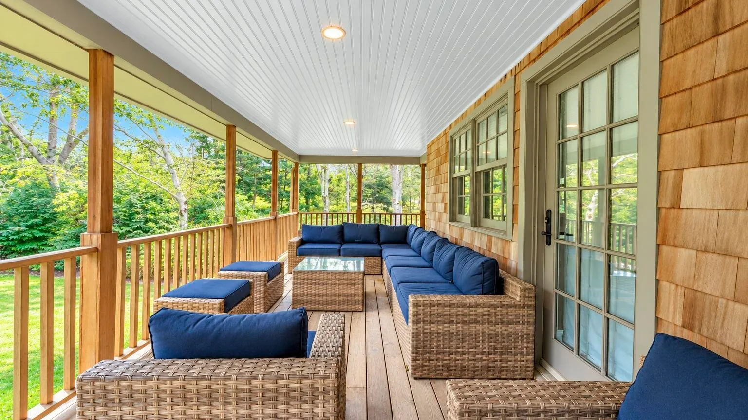 A covered porch with wicker seating and views of surrounding greenery.