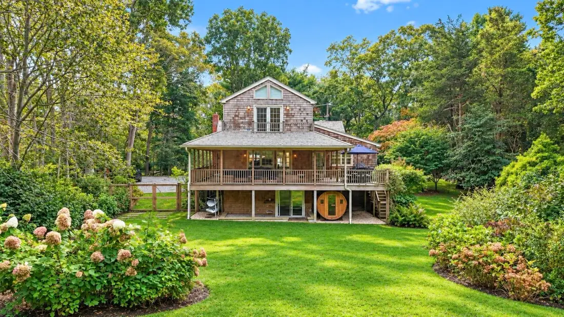 A wooded house overlooks a broad lawn, with a covered porch across the front.