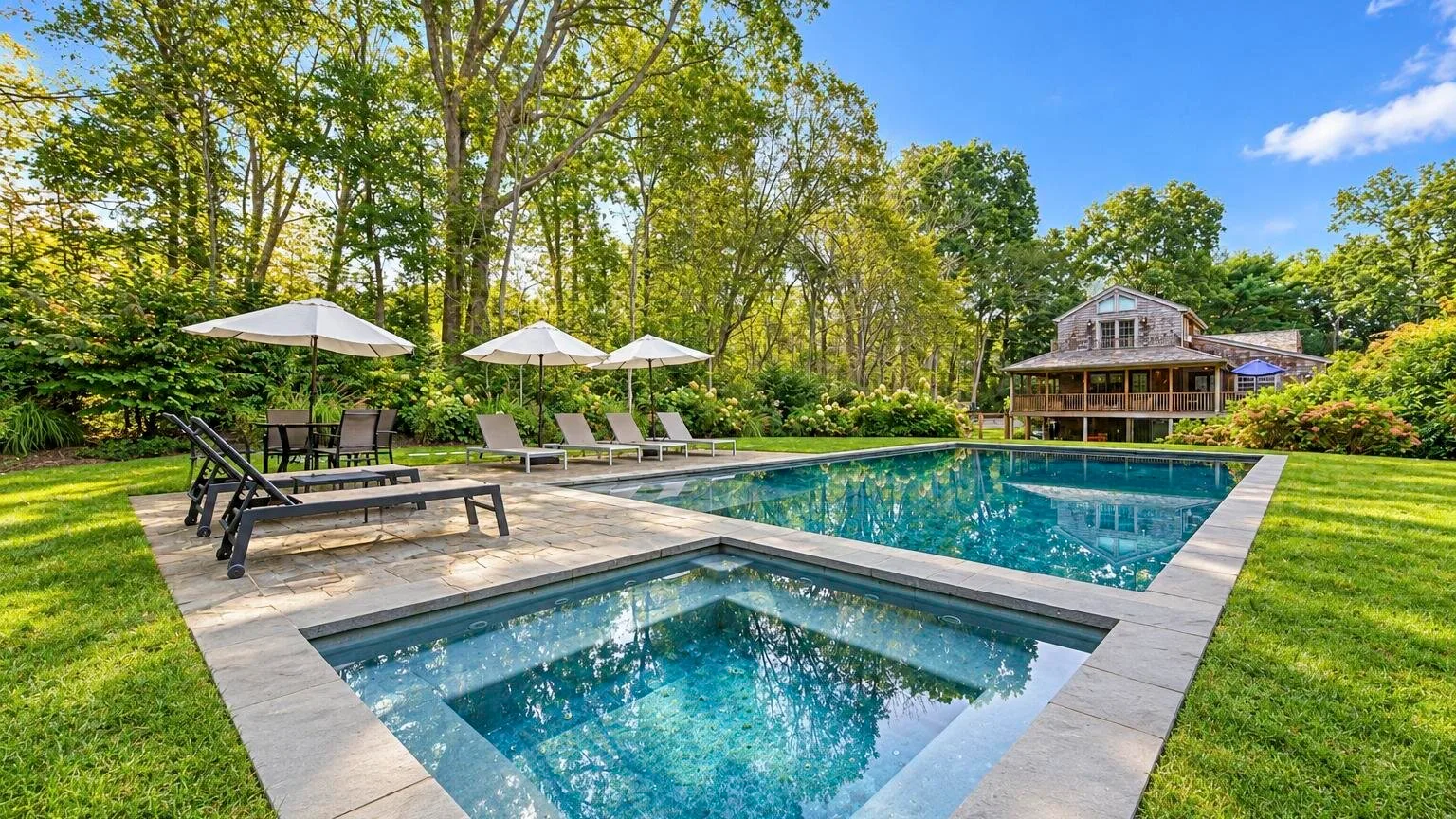 Una piscina al aire libre y un spa contiguo están junto a un césped arbolado y un patio.