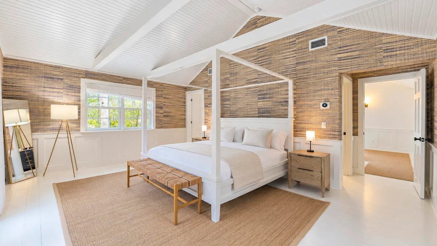 A bright bedroom with a canopy bed, bedside tables, and a large window.