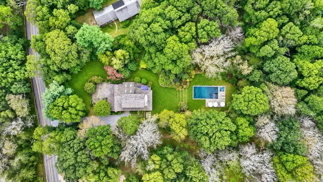 An aerial view shows a house, a swimming pool, and surrounding trees.