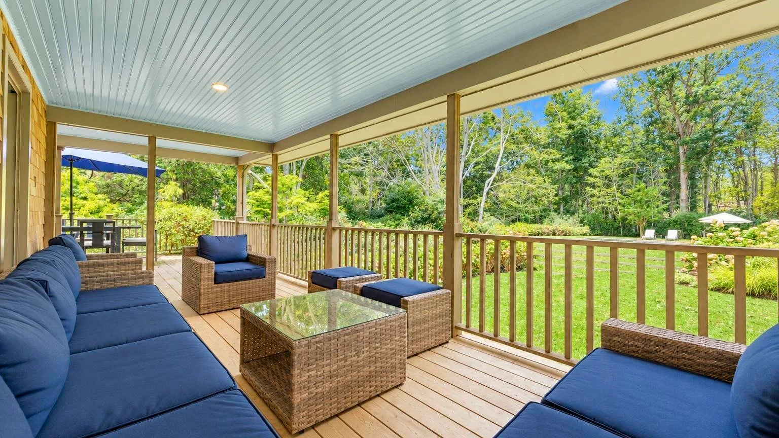 A covered outdoor seating area with cushioned furniture and a wooded view.
