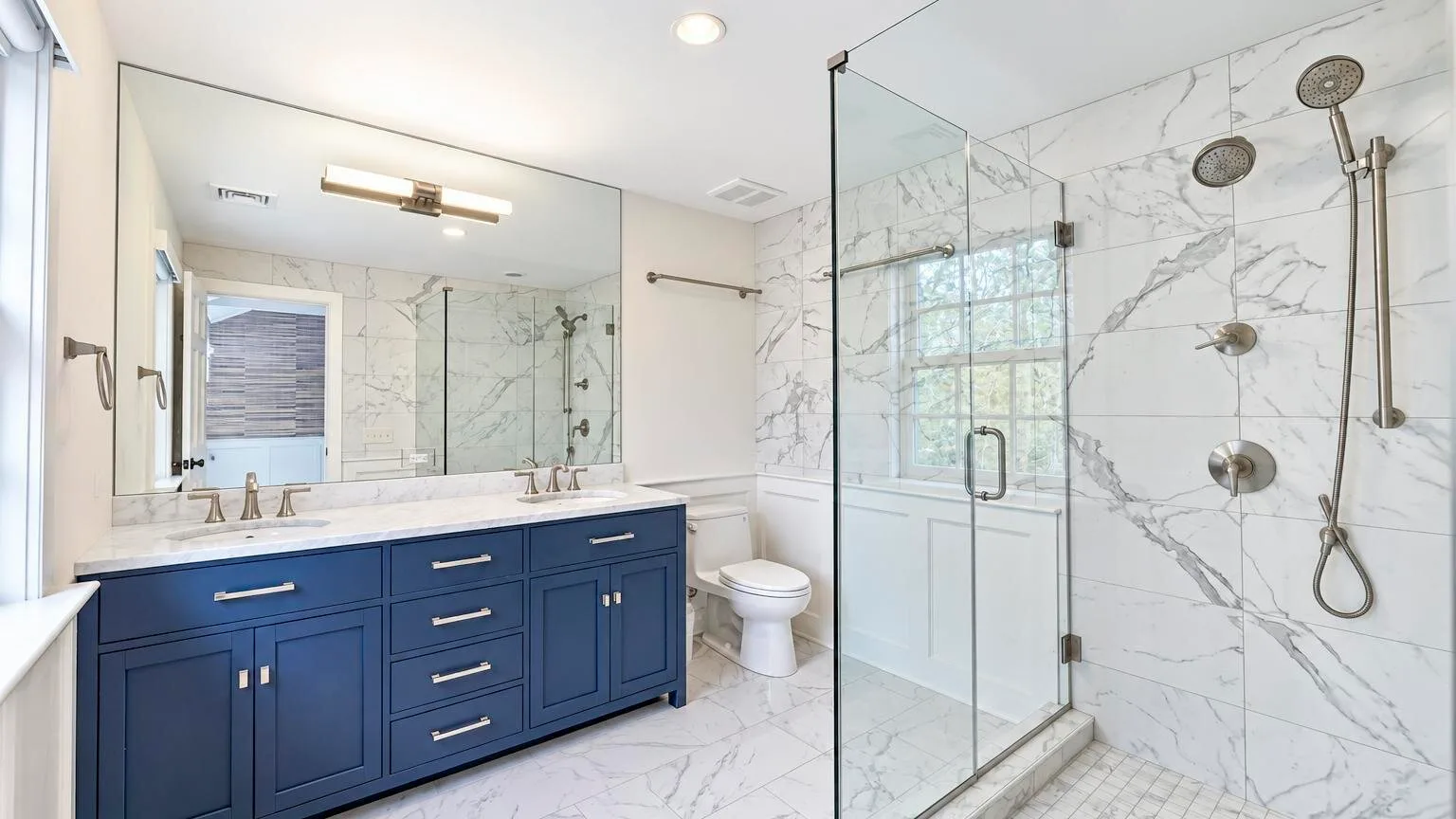 A bright bathroom with a blue vanity and a glass shower.