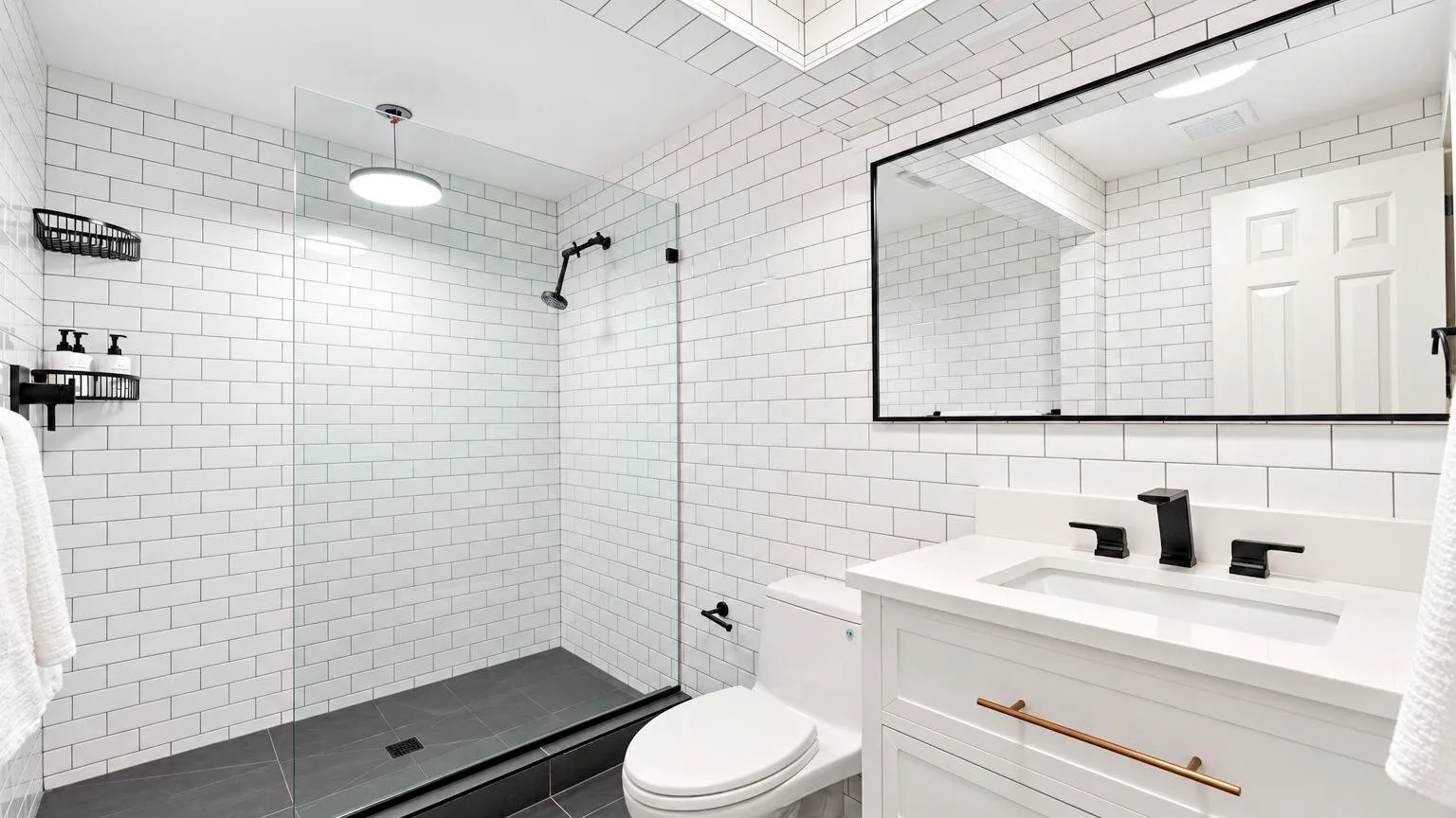 A bright tiled bathroom with a glass shower, toilet, and vanity.