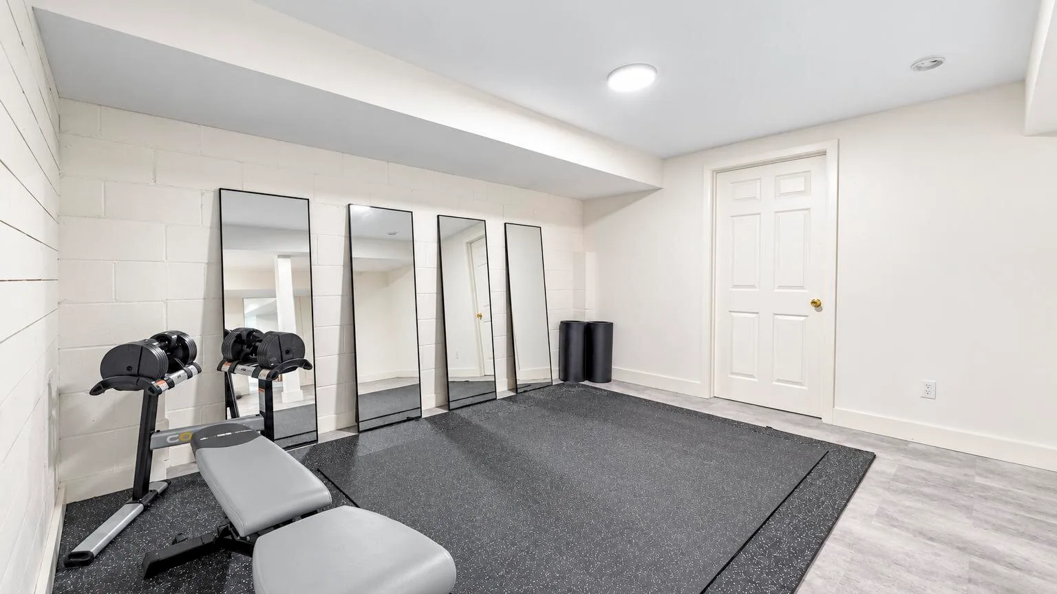 A basement workout area with exercise equipment, mirrors, and floor mats.