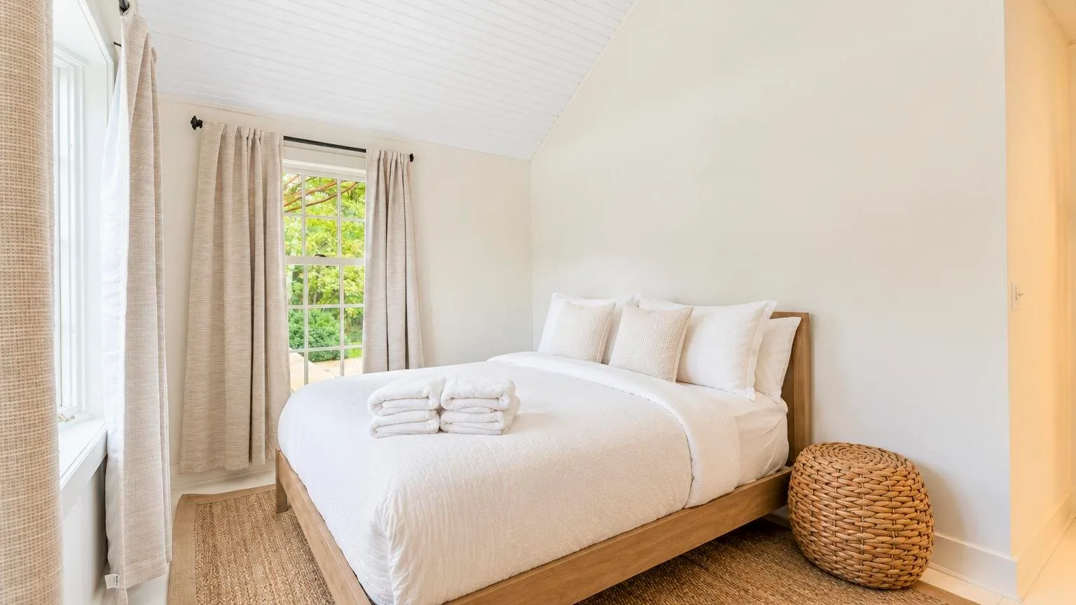A bright bedroom with a neatly made bed and curtained windows.