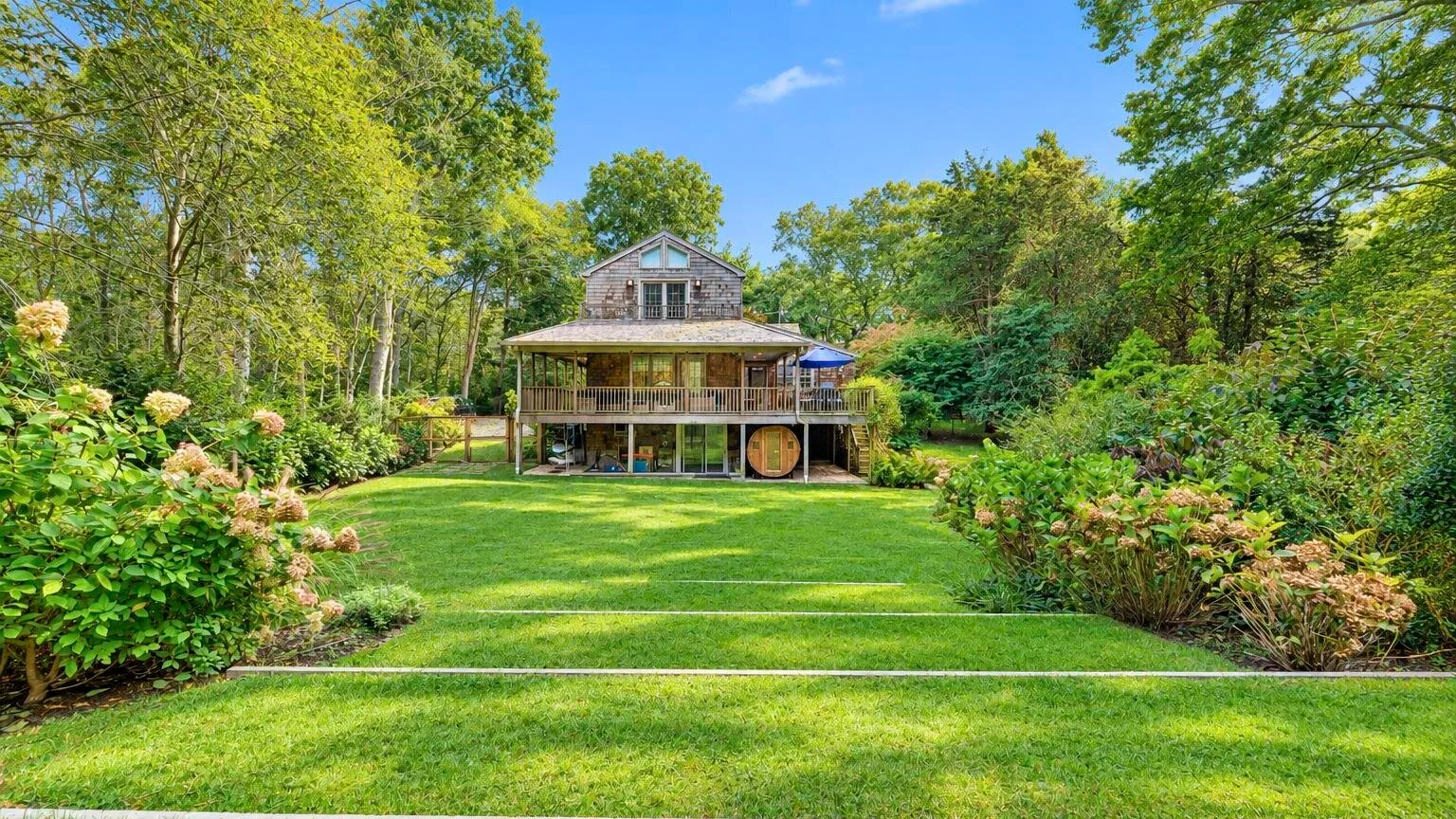 A large house stands beyond a broad green lawn, surrounded by trees and shrubs.