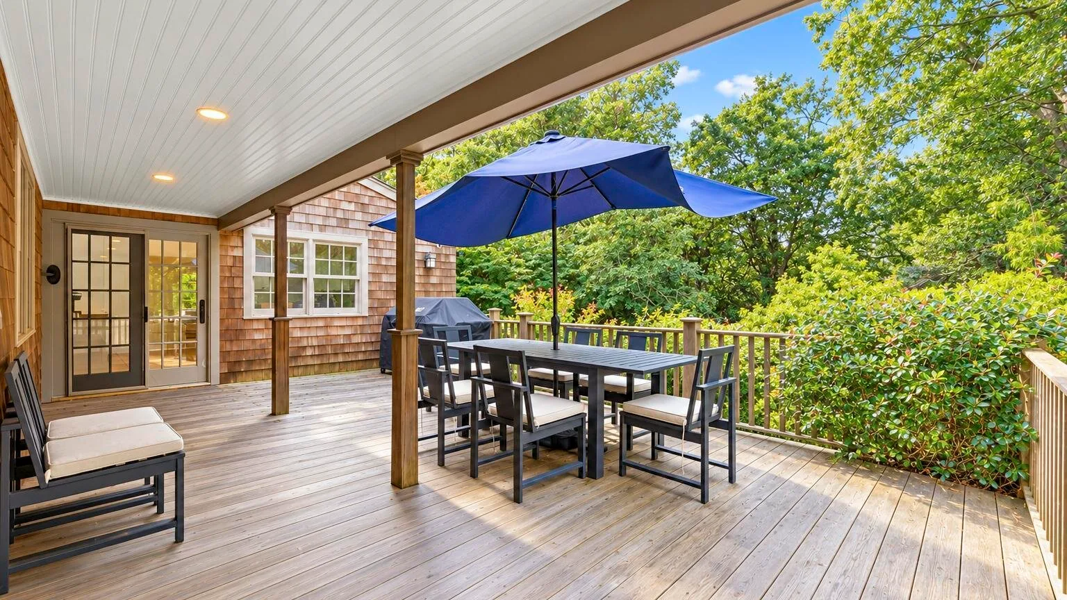 A covered wooden deck with outdoor dining furniture and a blue umbrella.