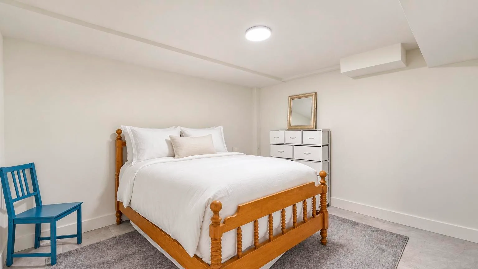 A bedroom with a wooden bed, white bedding, and a blue chair.