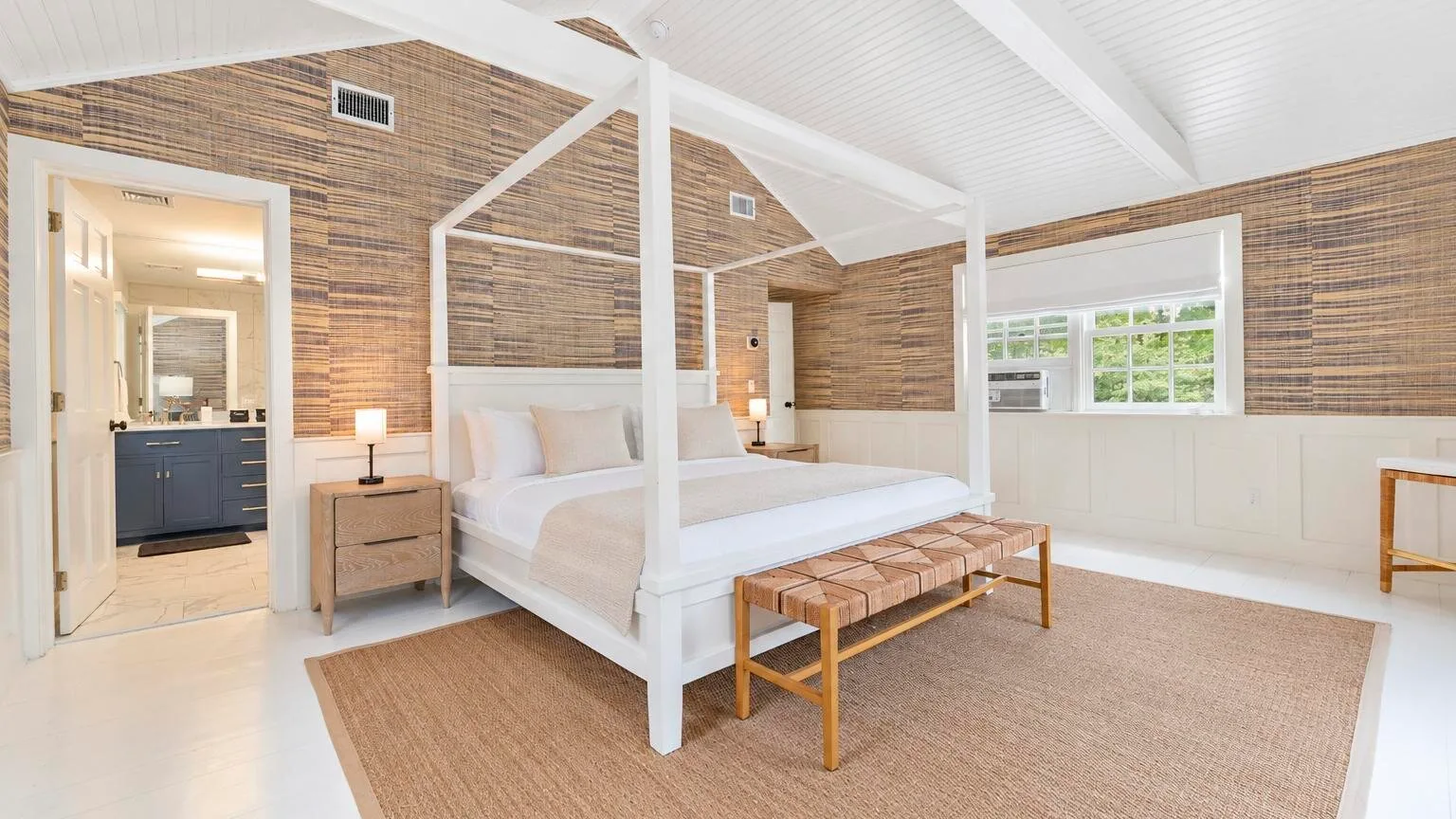 A bright bedroom with a white canopy bed and woven bench.