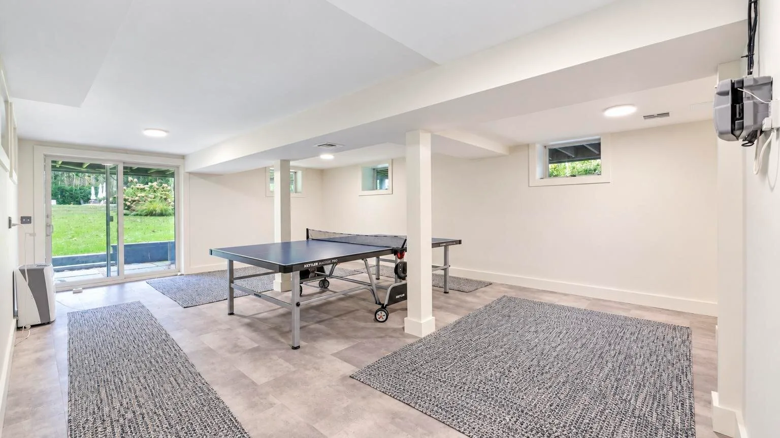 A basement recreation room with a ping-pong table and sliding glass doors.
