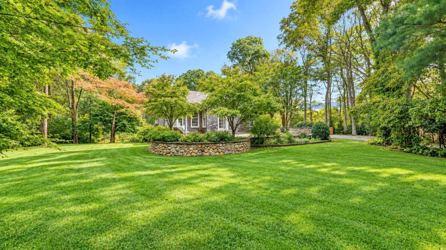 A broad green lawn stretches across a landscaped garden with mature trees.